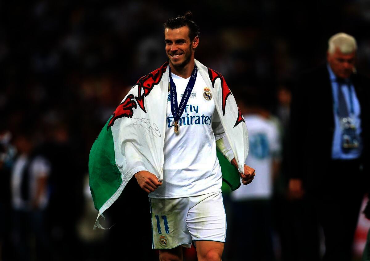 Welsh footballer Gareth Bale holding a Welsh flag while celebrating with football club Real Madrid.