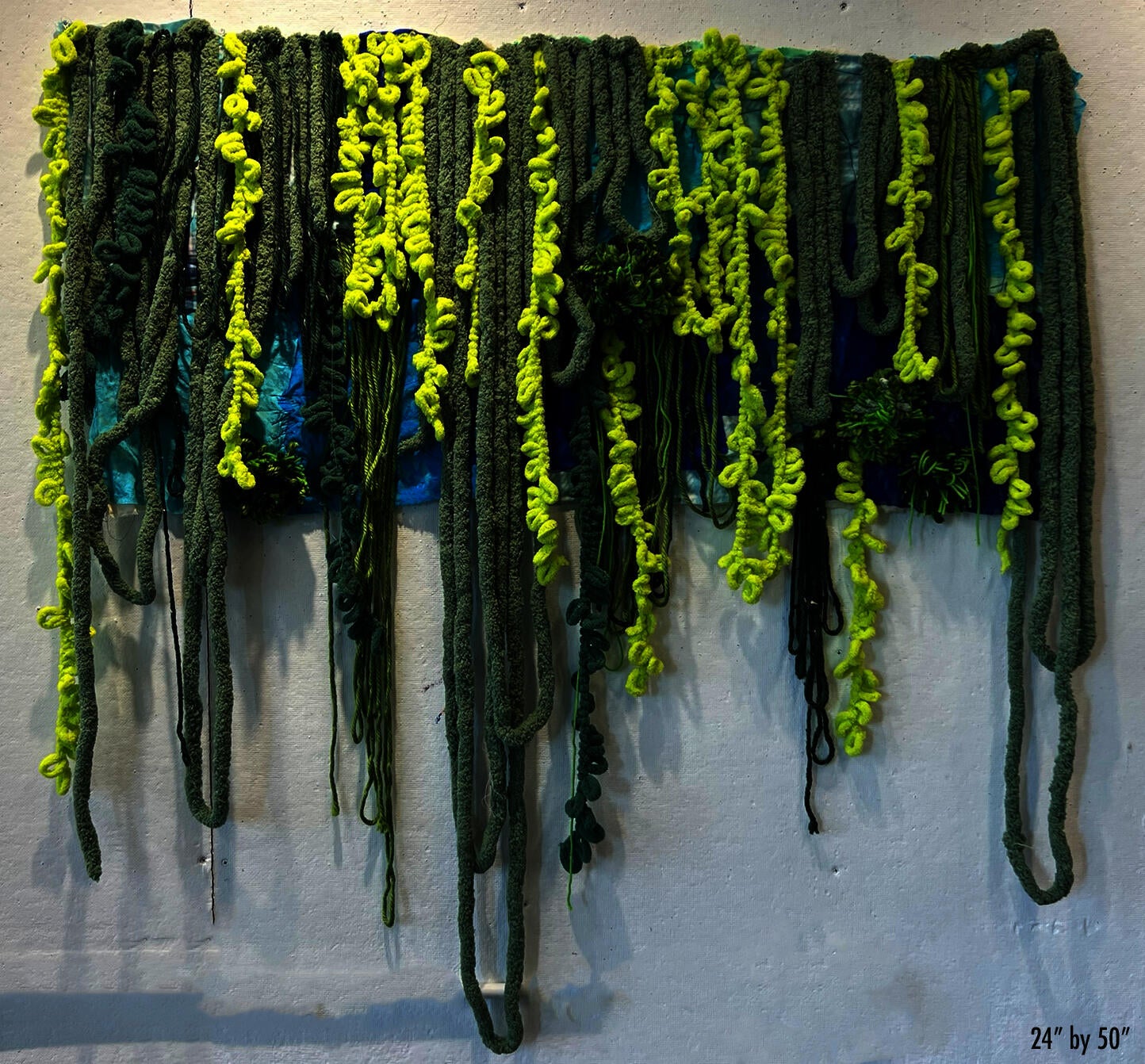 Blue textile rectangular with long thick green yarn strands dangling like vines