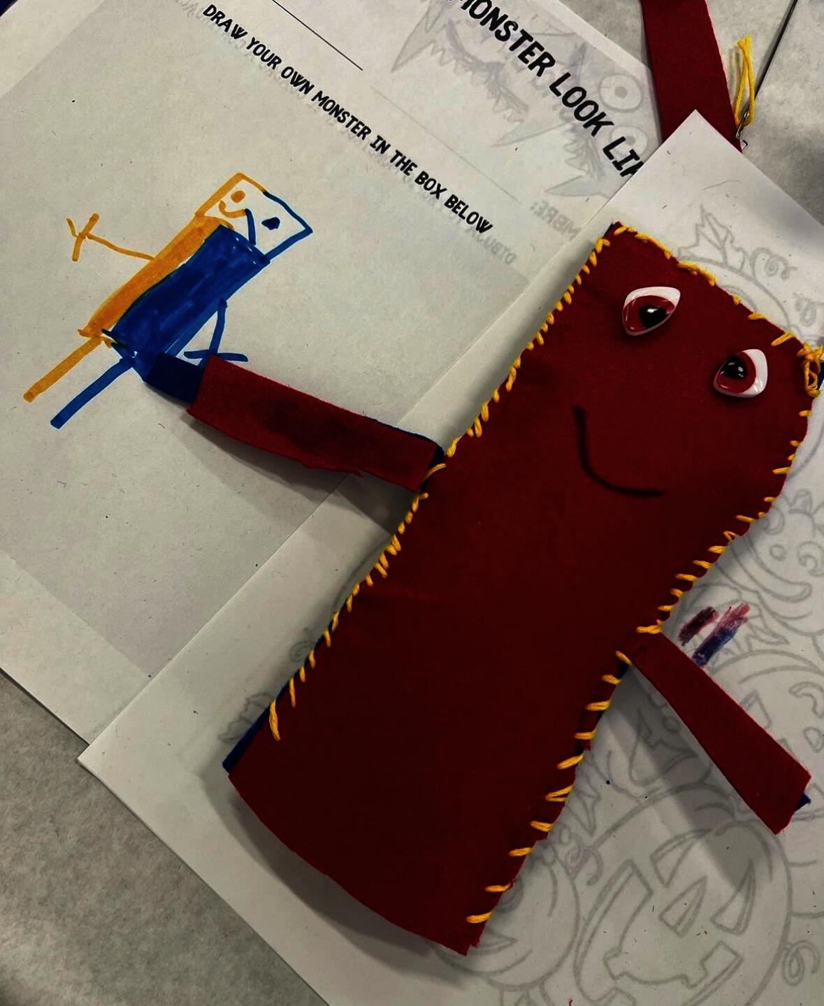 Red hand sewn color monster with red eye and yellow stitching around the rectangular body