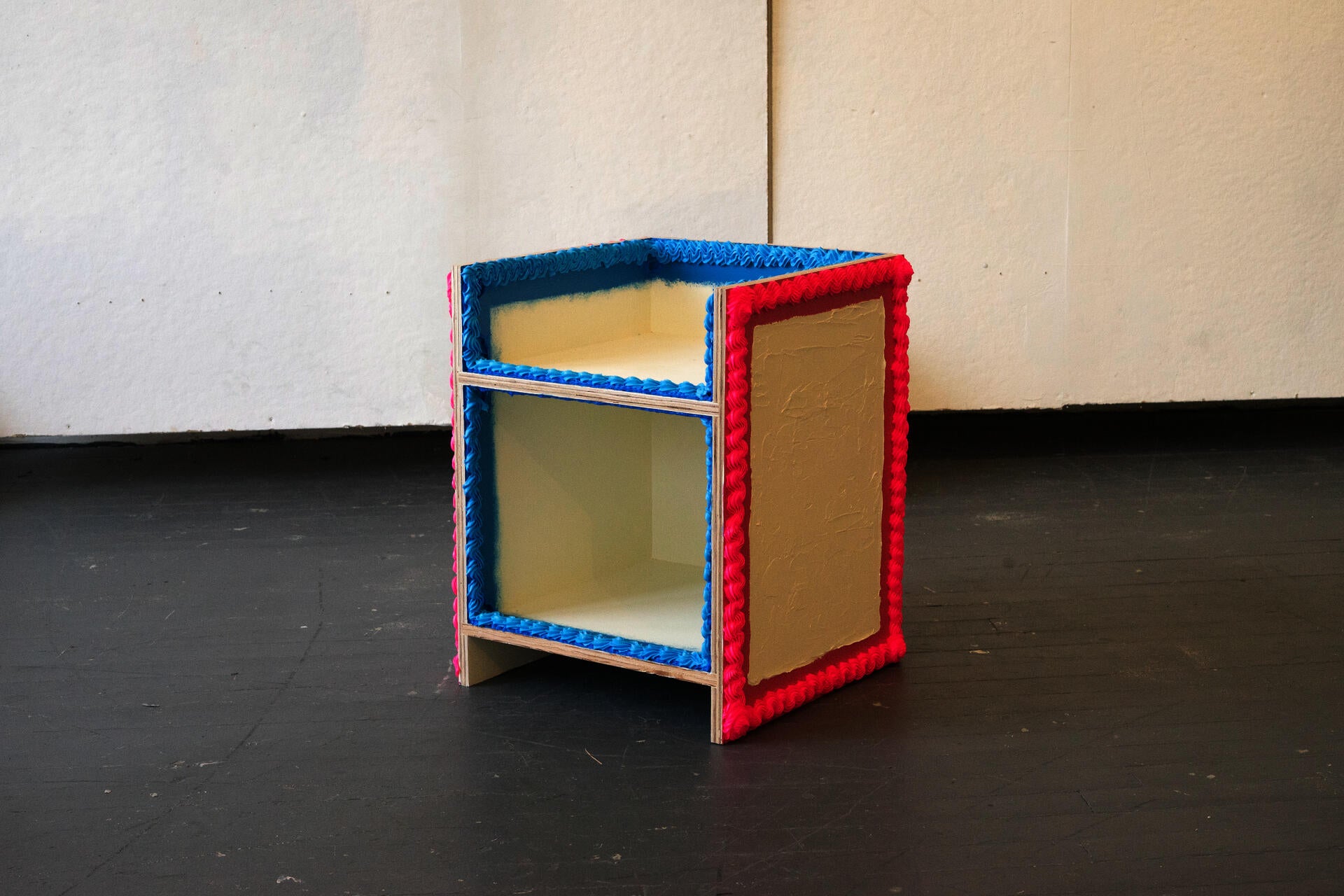 A lounge chair with a minimalist form painted in a buttercream color, decorated with blue and pink thick impasto style paint.
