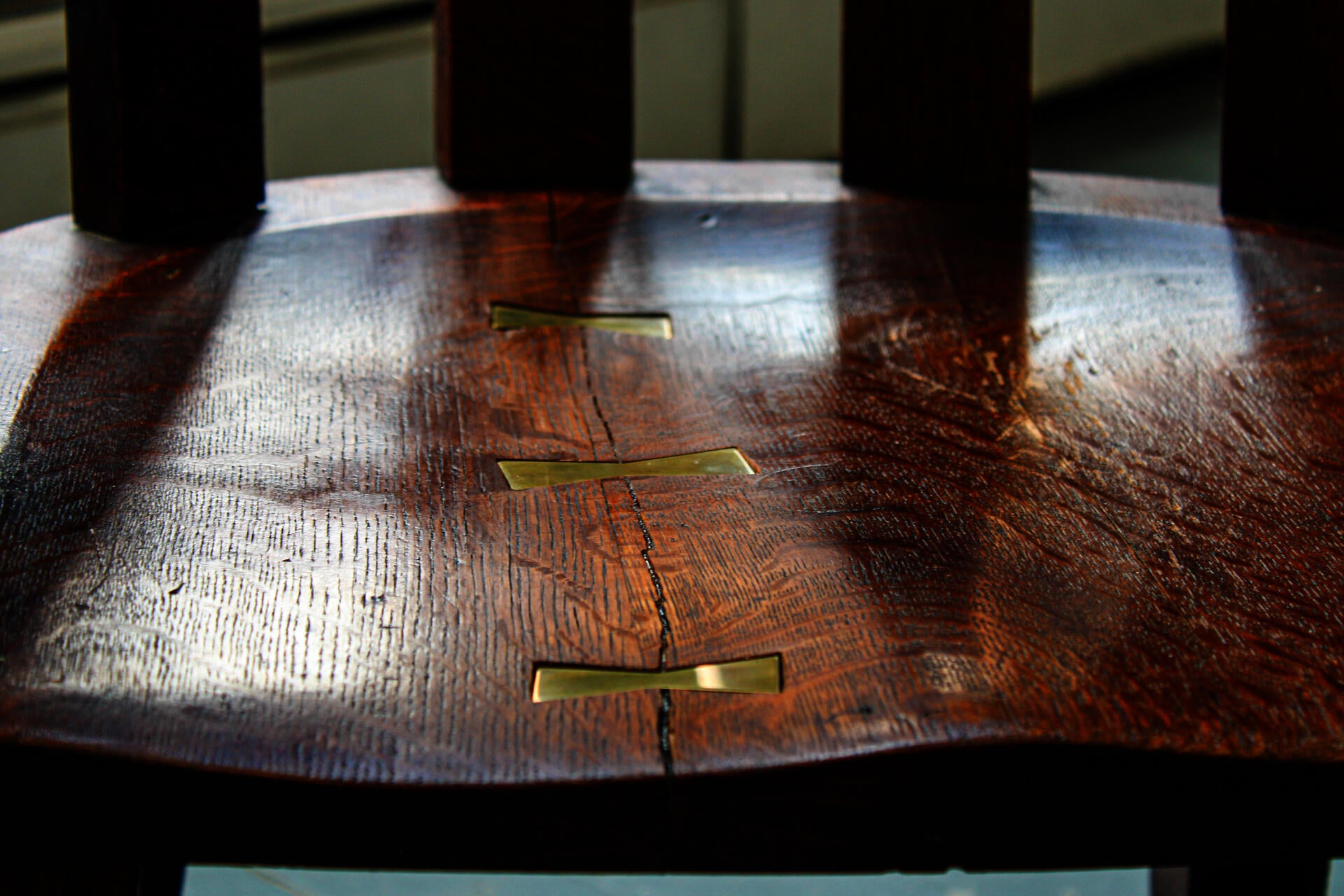 A close up shot of the repaired oak chair highlighting the brass bowties holding together the formerly cracked seat of the chair.