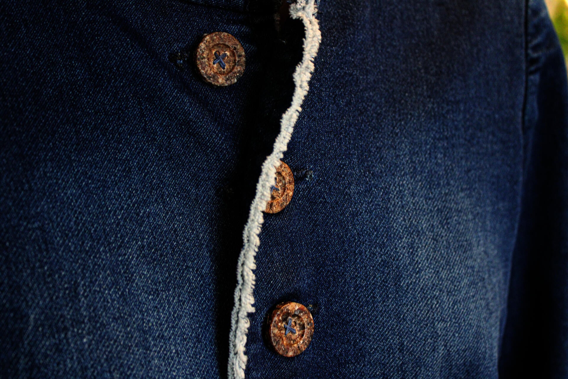 A close-up shot of three buttons made of periwinkle shells ground up and casted back together into the shape of a traditional button. They are stitched with blue thread onto a denim jacket.