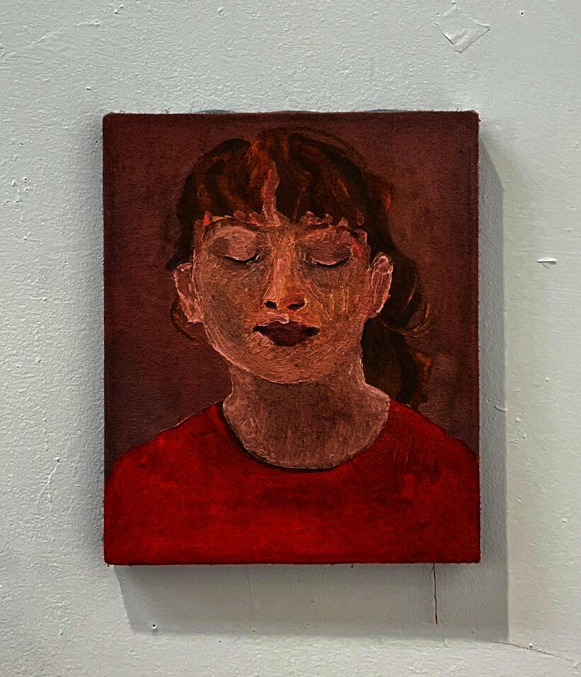 Portrait of a young woman from the neck and shoulders up. She is wearing a red shirt and has her eyes closed, chin tilted slightly upwards.