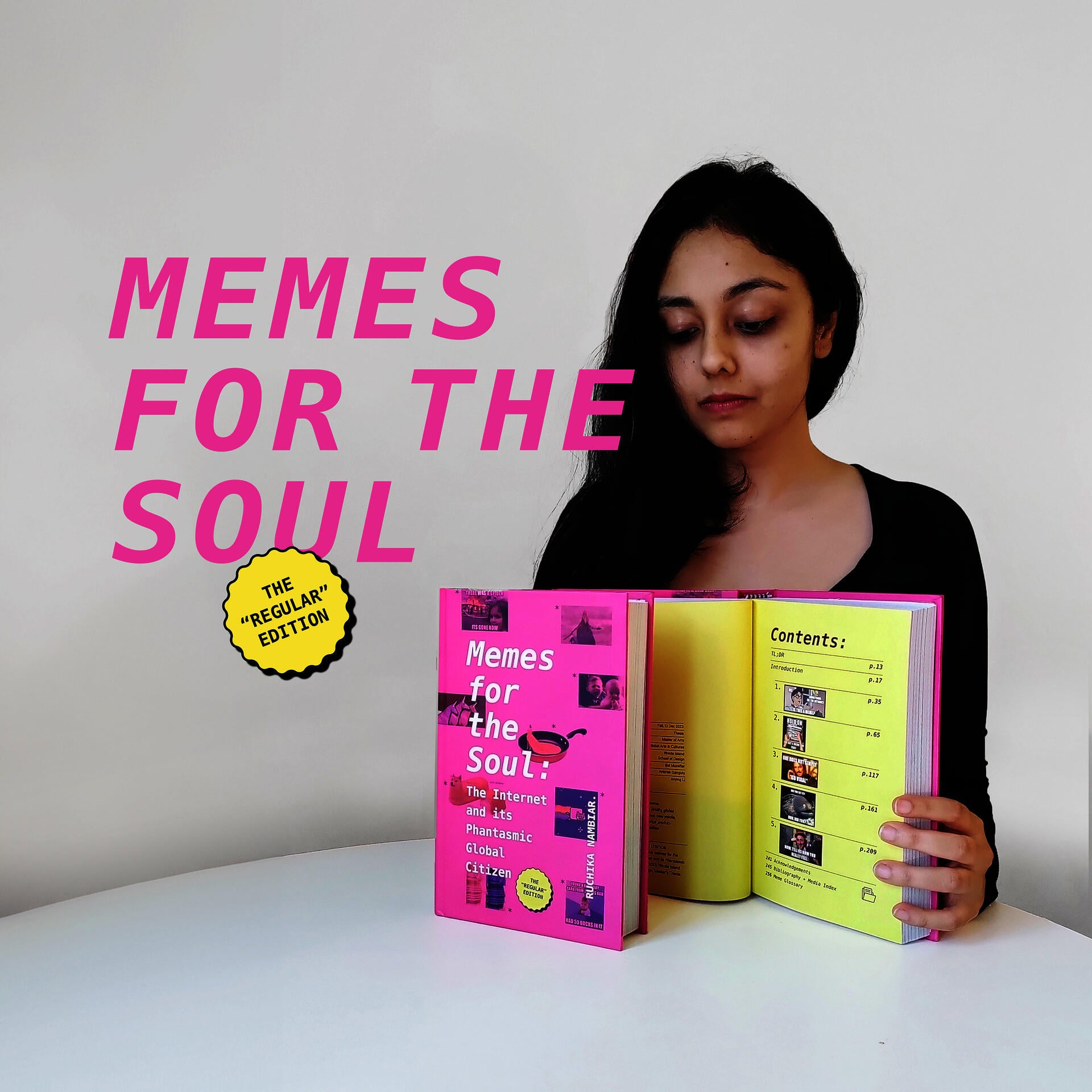 Ruchika Nambiar seated at a table with two copies of a hardcover book propped up in front of her. She is holding one of the books open to display its interior pages.