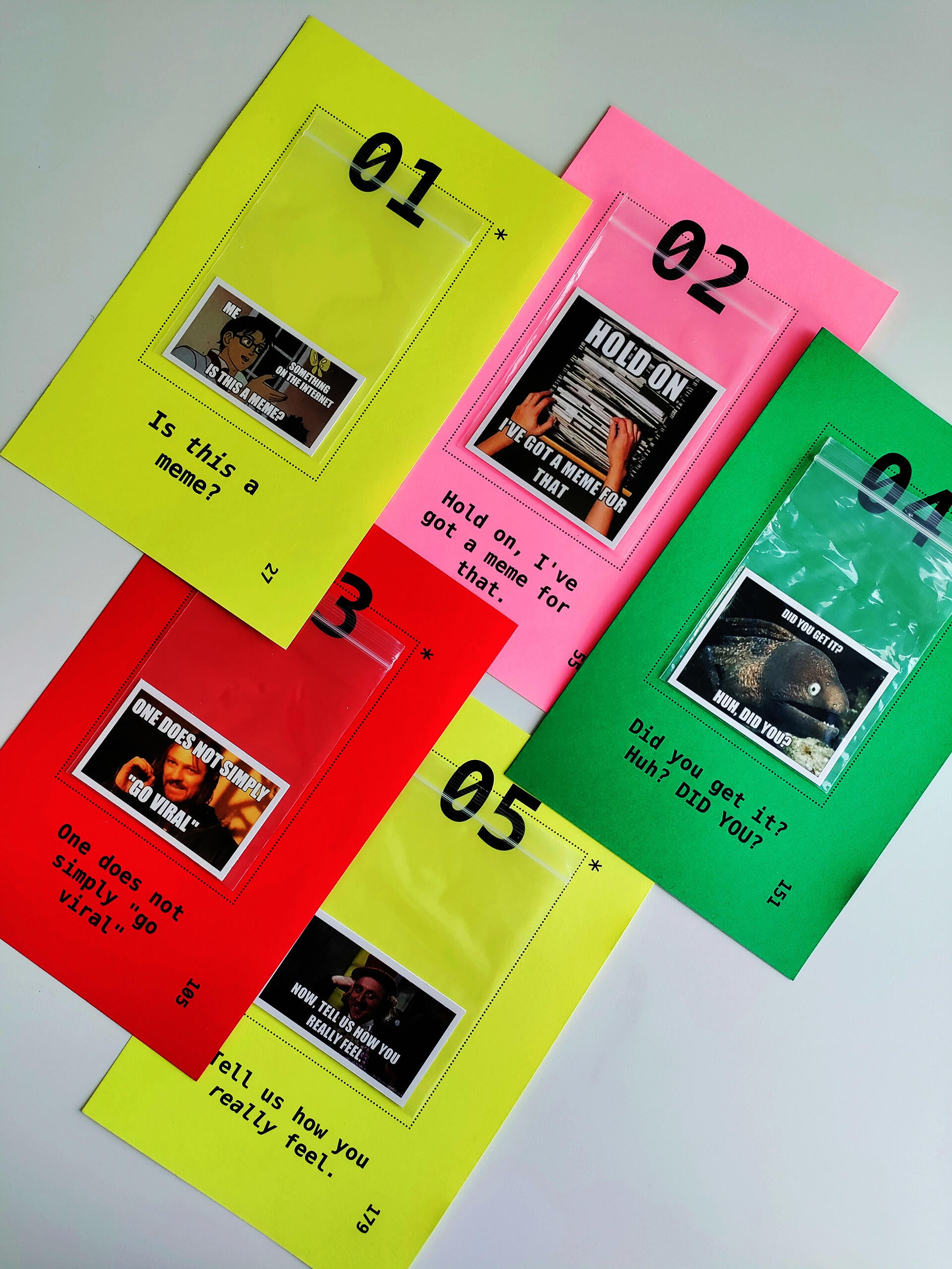 Five colorful loose pages printed with chapter numbers and titles. Each page has a ziploc bag attached to it, inside which is a printout of an internet meme. 