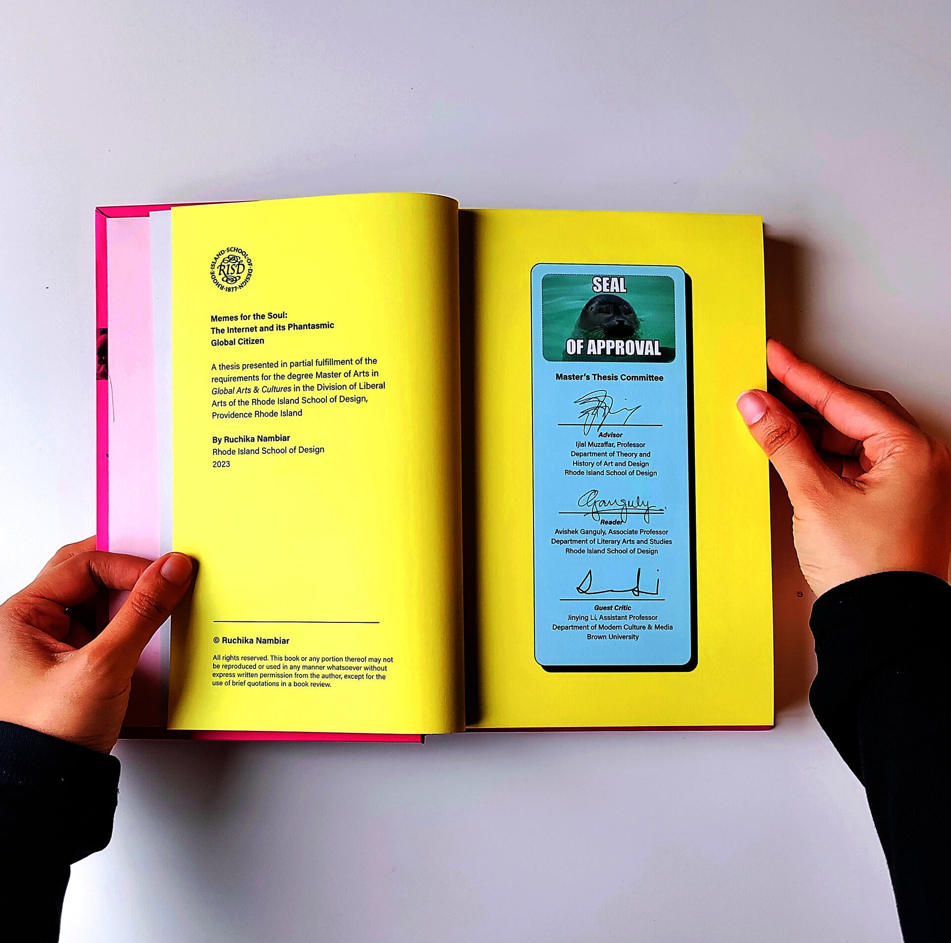 A hardcover book held open by a pair of hands to show two of its pages.