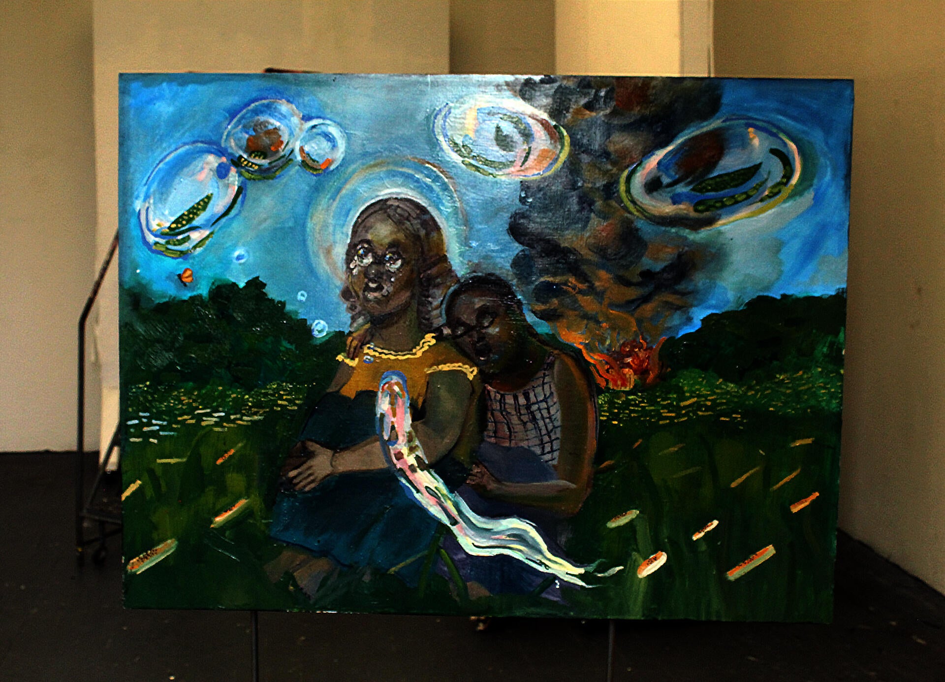 A larger rectangular oil painting on board, supported by a metal structure. The painting depicts two girls sitting in front of a burning house as bubbles float by.