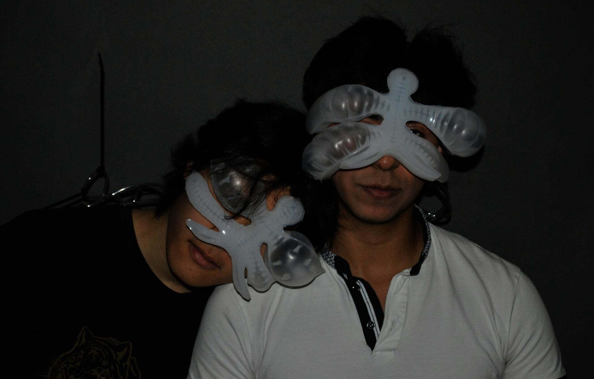Dylan and Brandon, one leaning on the other's shoulder, adorning chimera, a soft robotic entity that sits on the face. The augmentation is inflated reflecting their emotion.