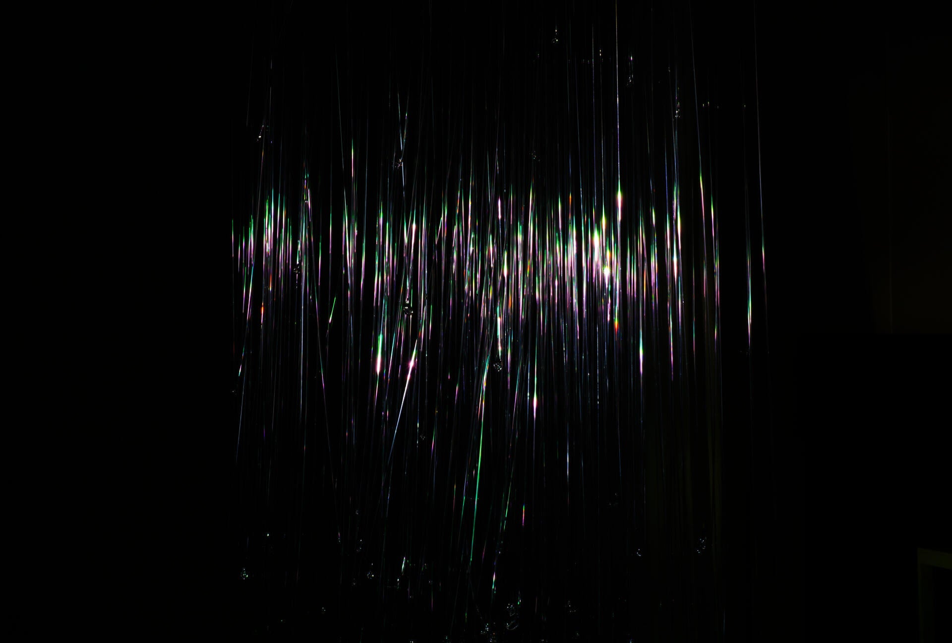 Hundreds of glass fibers suspended in the room, with iridescent light reflected on the surface
