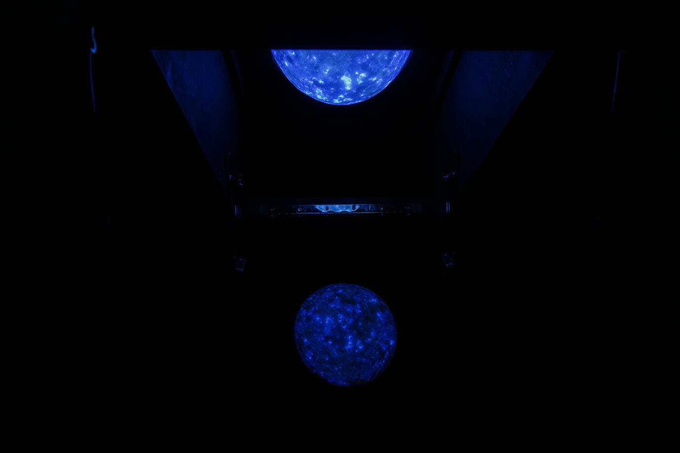 A fluorescent blue moon appears in a dark room, reflecting off an angled acrylic sheet, creating a captivating and ethereal visual effect.
