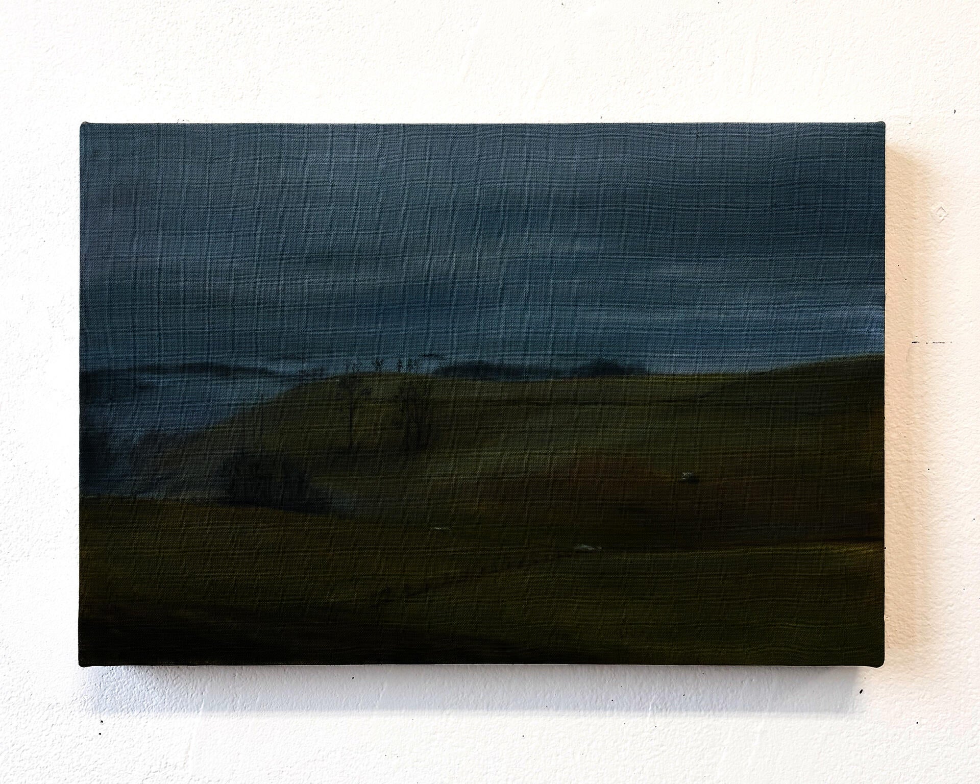 This is a landscape painting of rolling hills, seemingly in late winter. The sky is overcast, and fog has settled in the valley. 