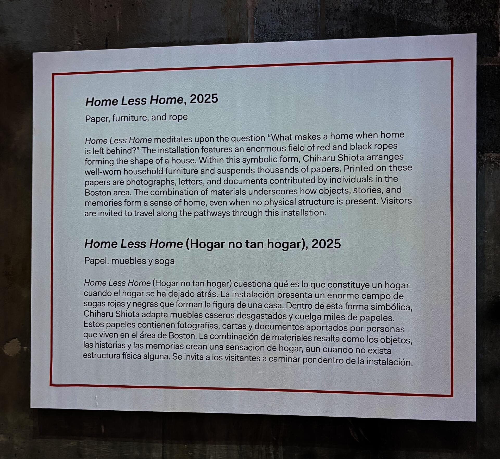 A large white label affixed to a concrete wall. The name of the work, the materials used, and a brief paragraph about the installation written in English; below, the name of the work, the materials used, and a brief paragraph about the installation written in Spanish. 
