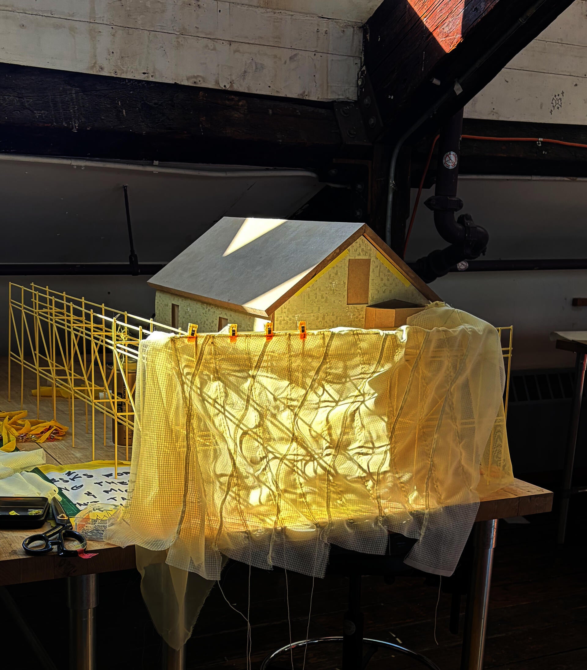 Layers of yellow fabric sewn and draped over scaffolding with house model behind. photo taken on studio desk