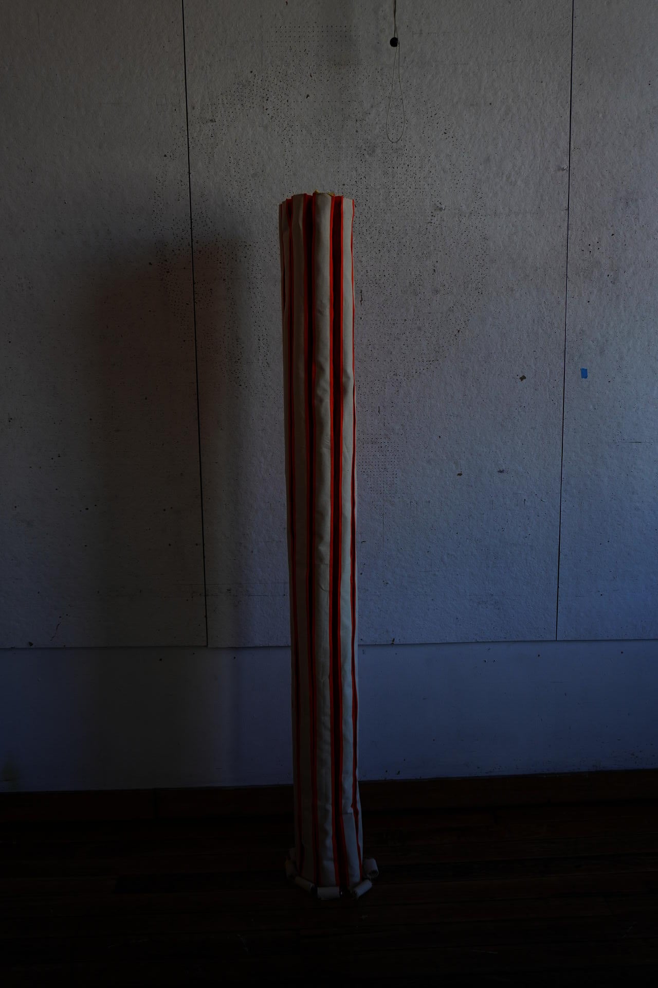 skinny fabric collumn standing on its own with orange stripes running from the floor to the top.