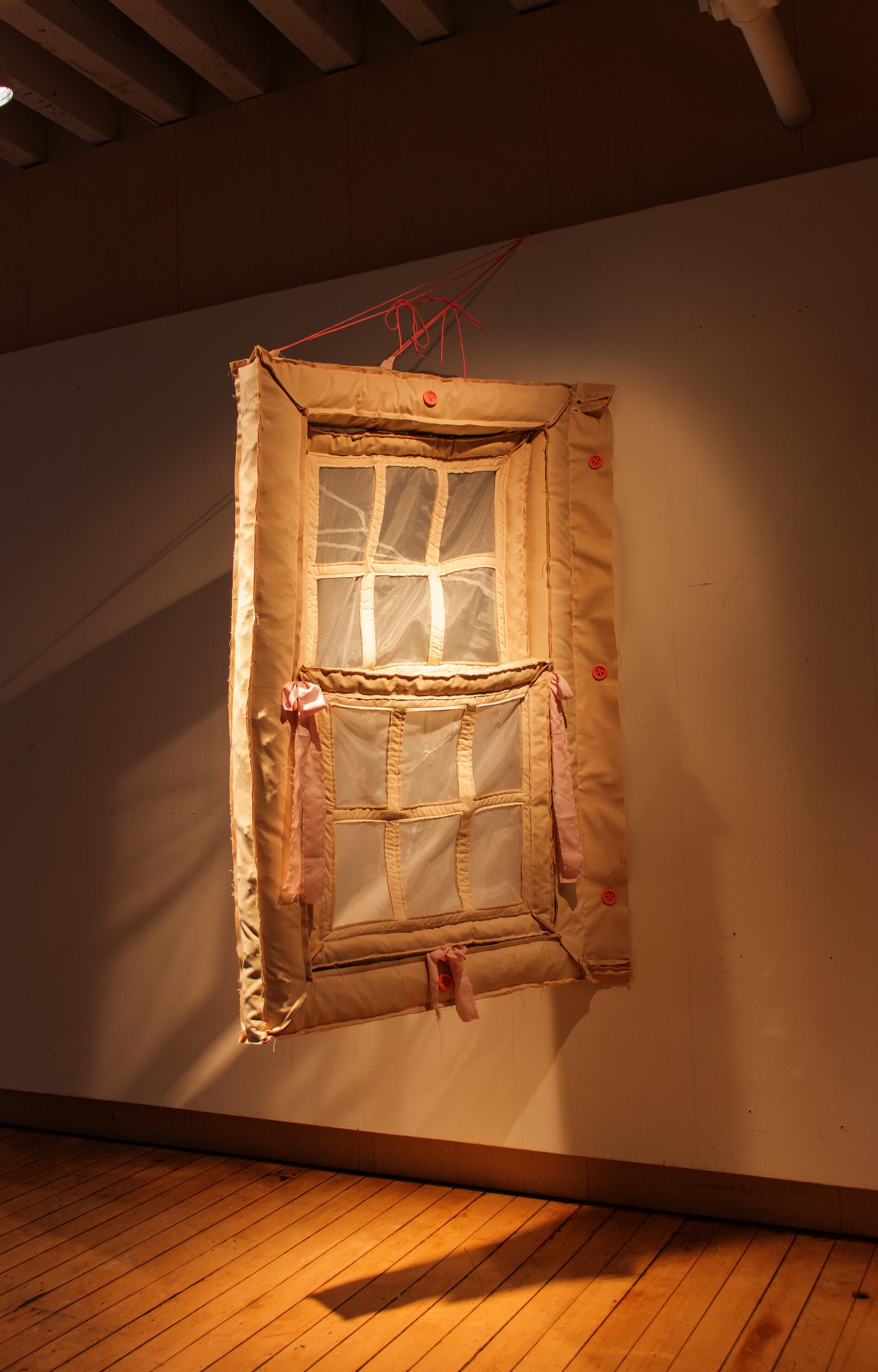 Hanging window made of off-white canvas fabric. 3 large pink buttons attach it to the wall.