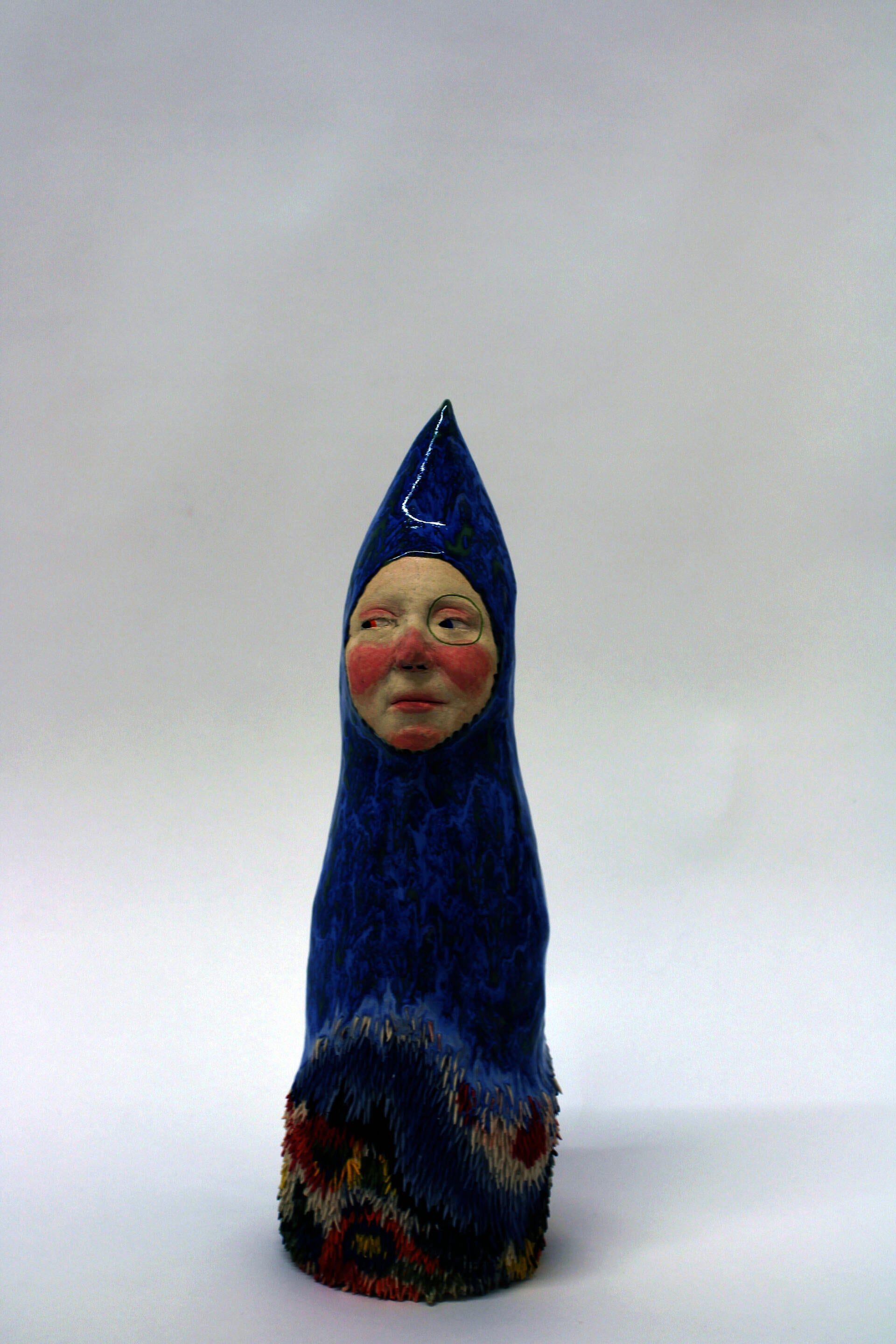 A blue and green small monolithic figure, with its face being a sort of flesh-colored window sticking out. There is some colorful fur at the bottom.