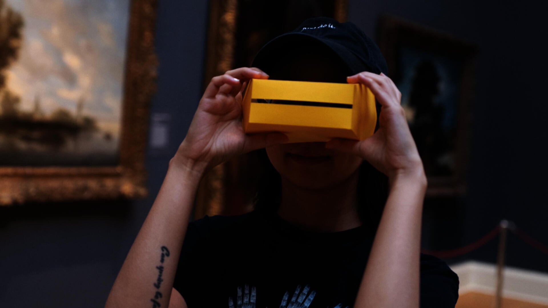 A person inside an art museum looking at the camera and wearing a yellow shape as glasses. 