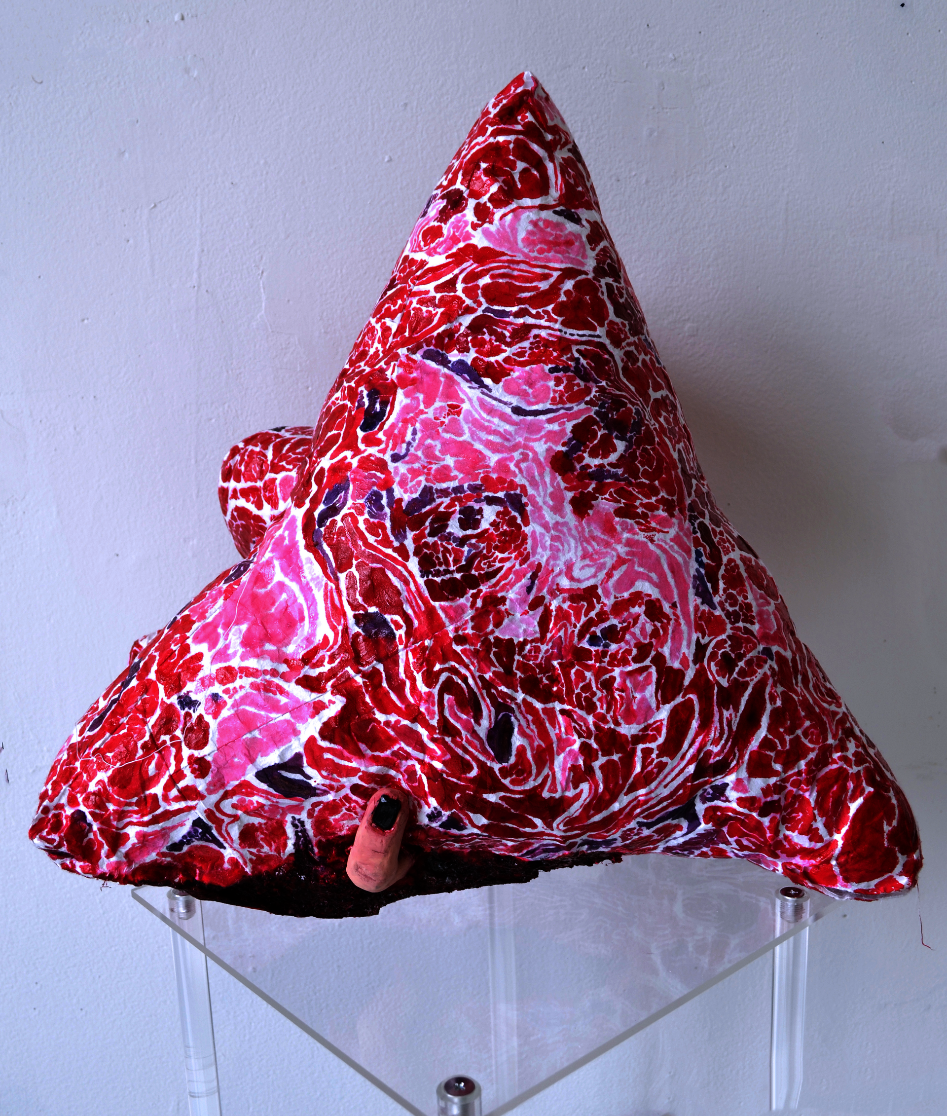 A triangular soft sculpture with a patterned painted surface mimicking a meat texture. 
