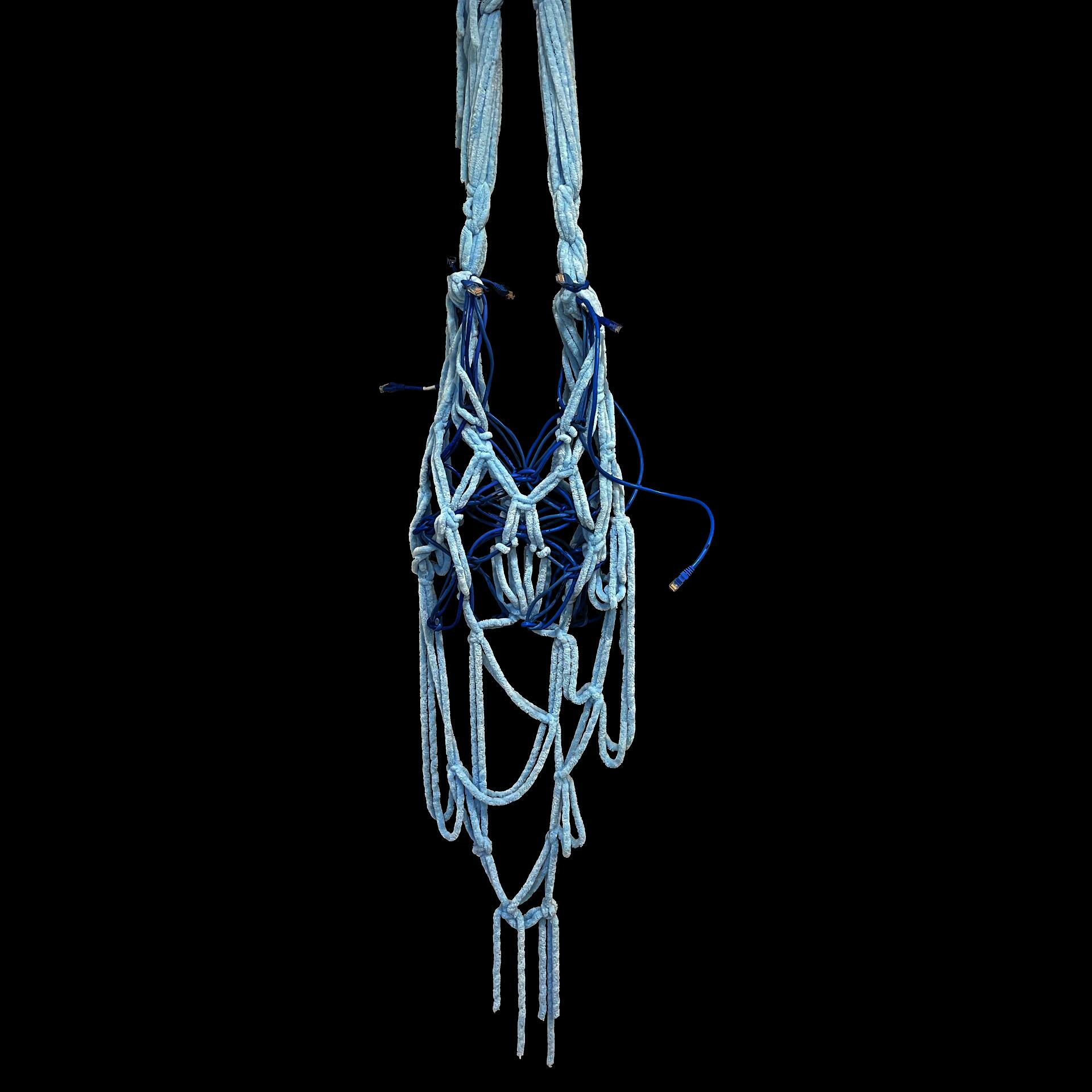 Hanging woven carrier bag made from blue fuzzy yarn and ethernet cables against a black background. Long looping strands and exposed cable ends contrast soft textile craft with rigid digital wiring, evoking entanglements between memory, technology, and physical objects.