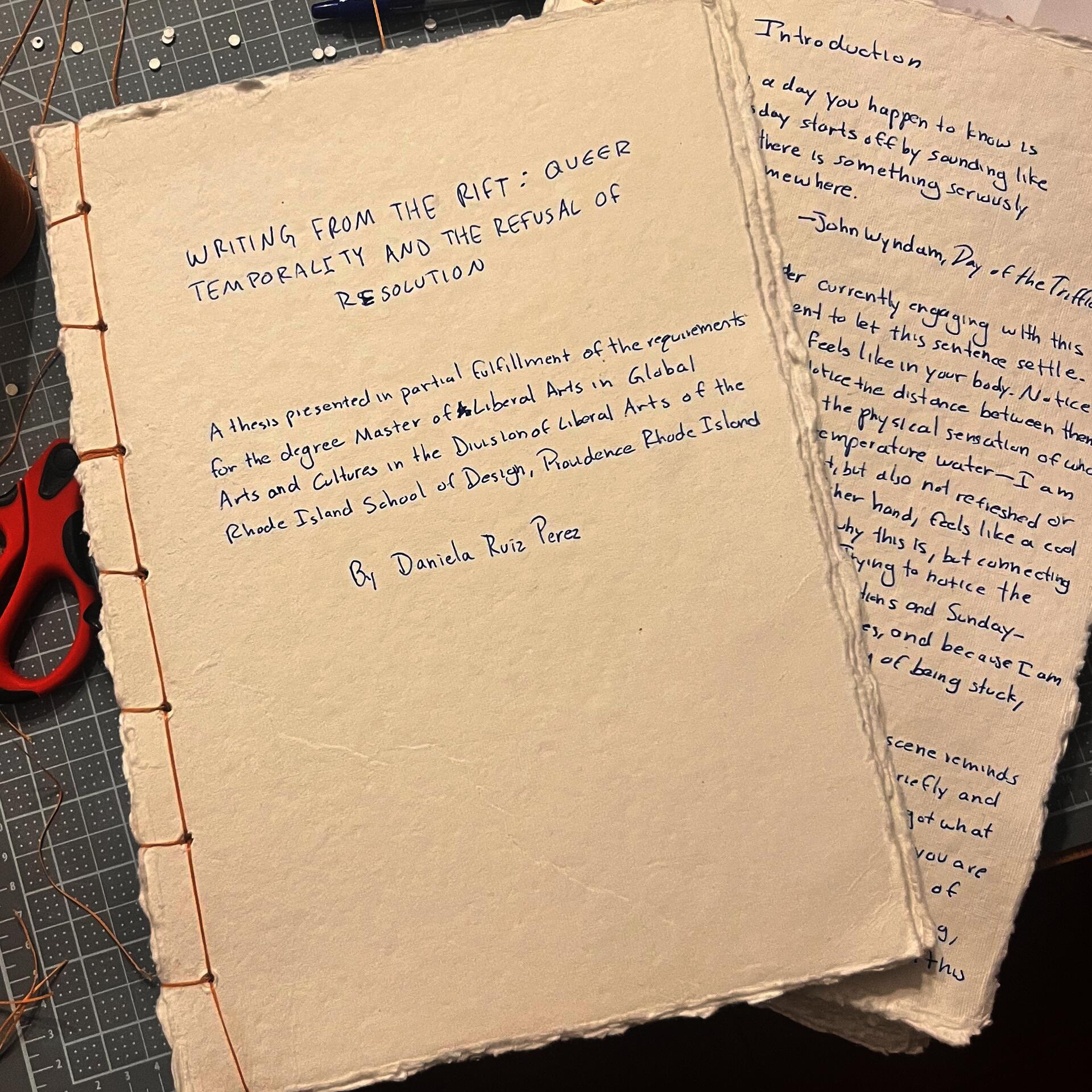 Hand-bound cream paper thesis manuscript on a cutting mat, stitched with copper thread along the left edge. Blue handwritten title reads “Writing From the Rift: Queer Temporality and the Refusal of Resolution.” Another handwritten page rests beside it.
