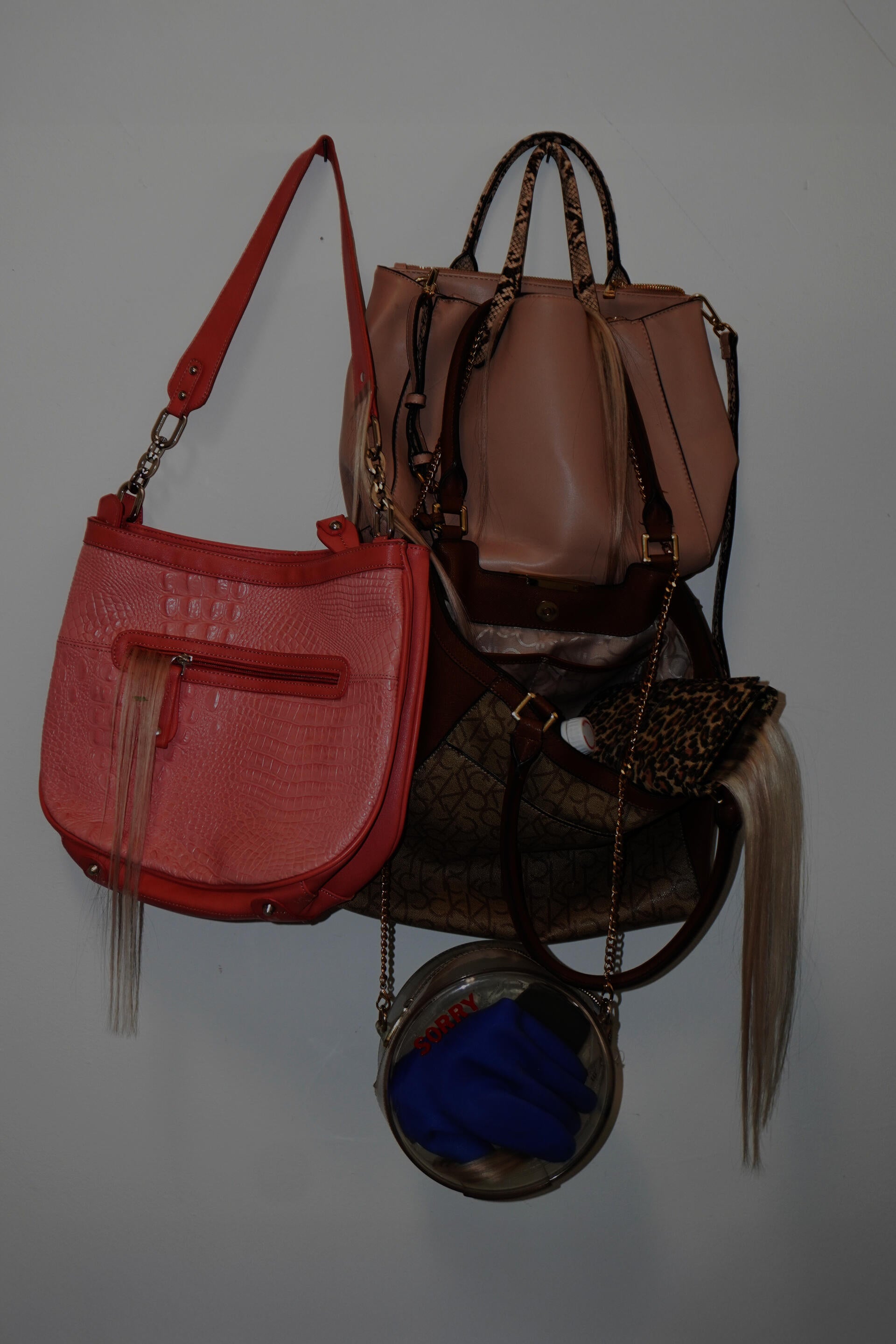 Stolen bags hang, hair coming out from the seams. Inside, a glove and a vinyl “sorry” sticker.