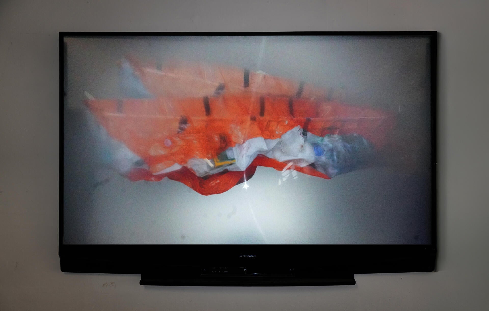 "A disassembled TV screen with a Fresnel lens. On the back, an archival paper print of the orange plastic boat sculpture, distorted through the lens. "