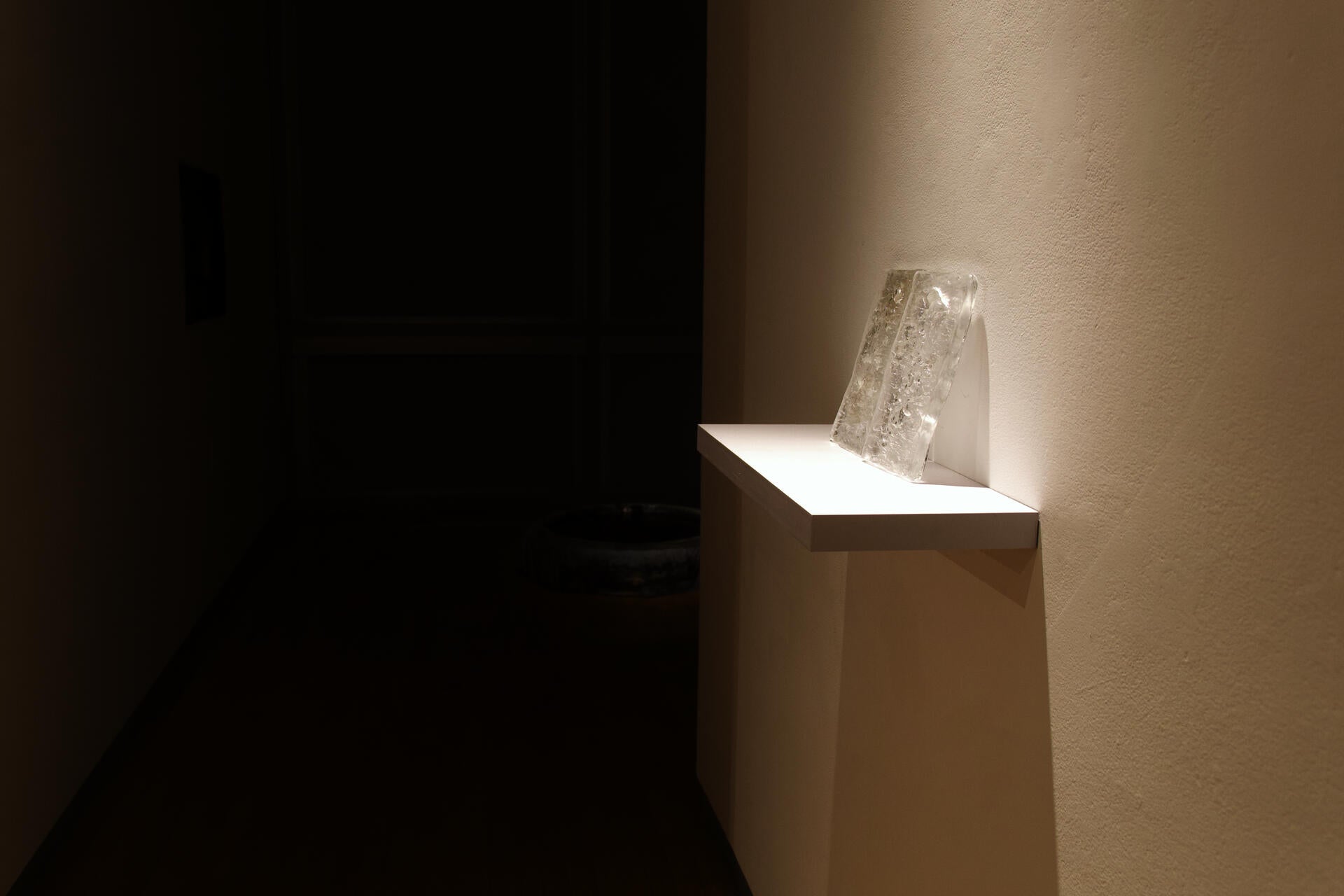 Dim installation view with translucent glass slabs on a white shelf and a dark water basin in the background.