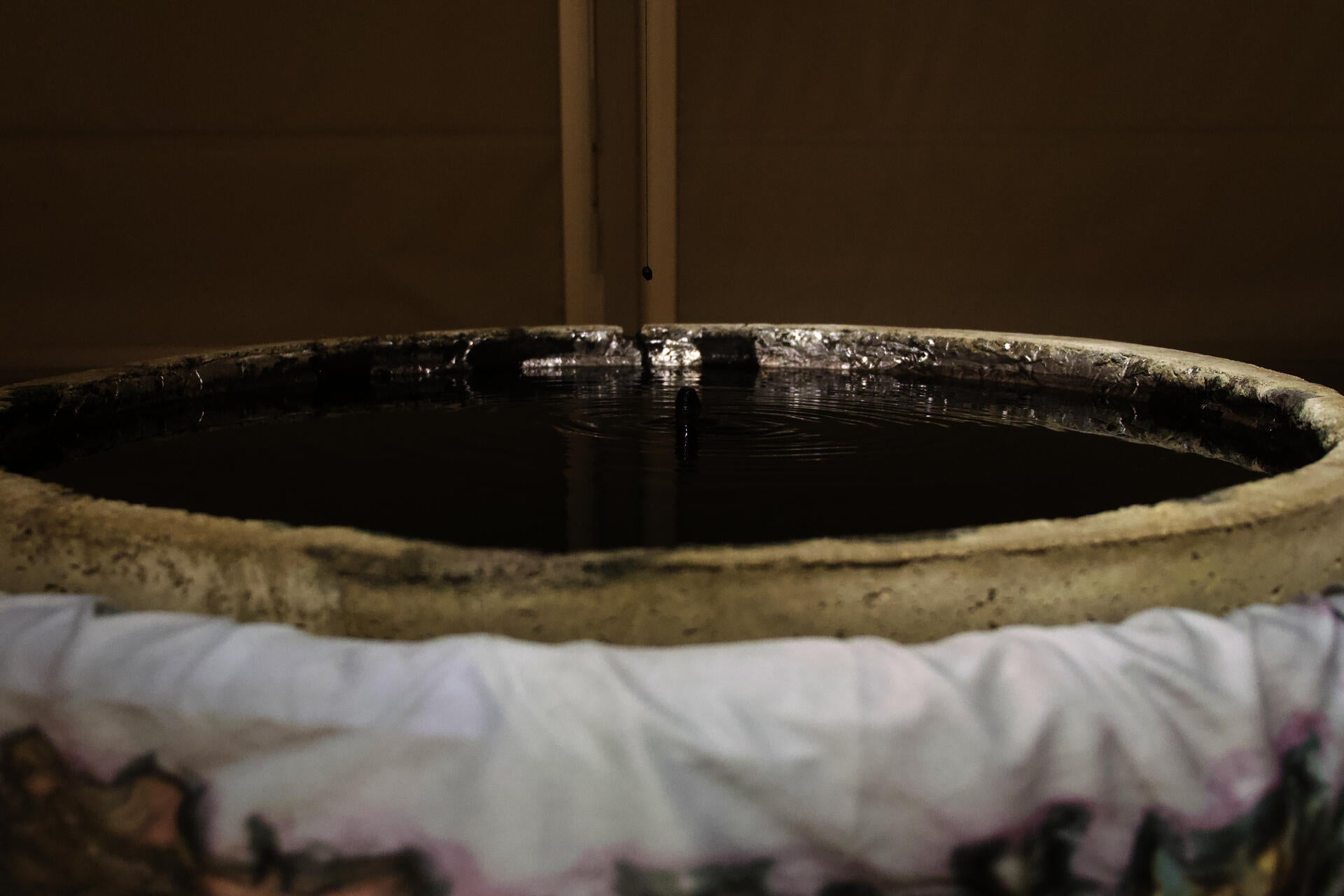 Close-up of dark rippling water in a concrete basin, with a small black bead suspended above the surface.
