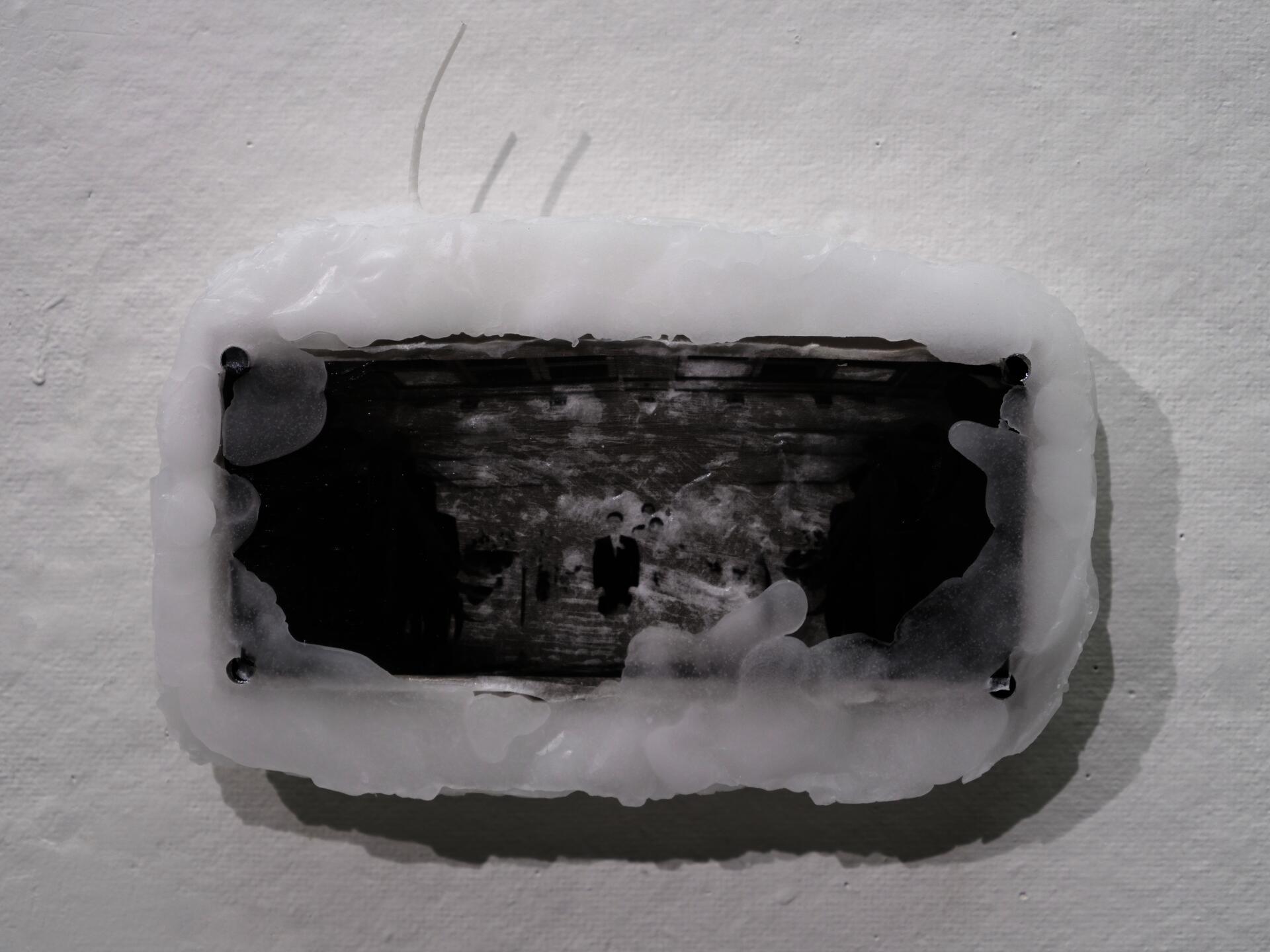 Close-up of a black-and-white family photograph partially covered in white paraffin and mounted on a wall.