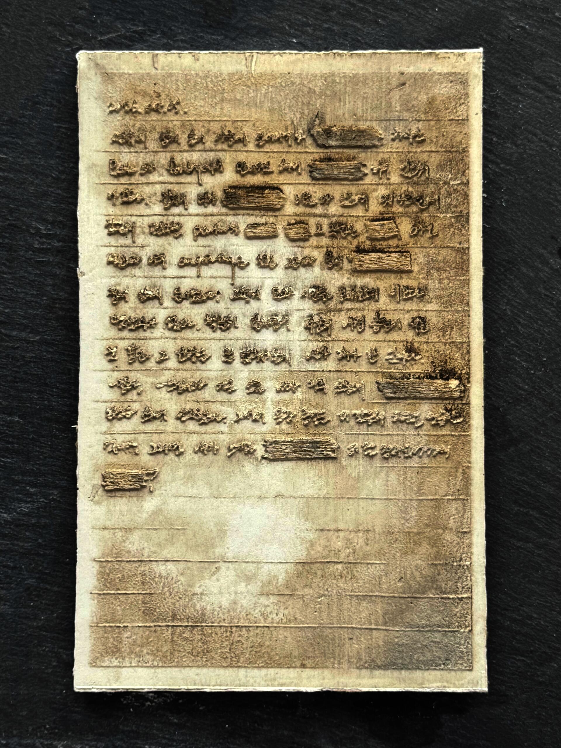 Close-up of a plaster page with raised handwritten text and redacted sections on a dark surface.