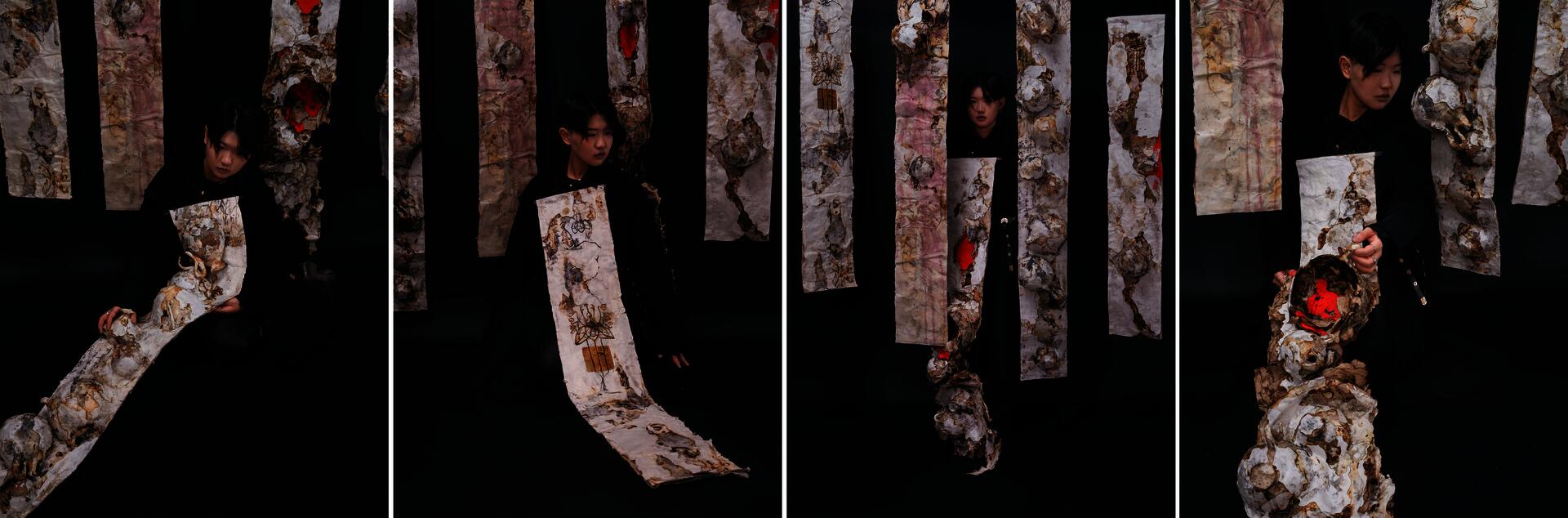 A model wearing scroll-like paper jewelry stands in a dark installation space surrounded by hanging scrolls with ink marks and layered paper textures.