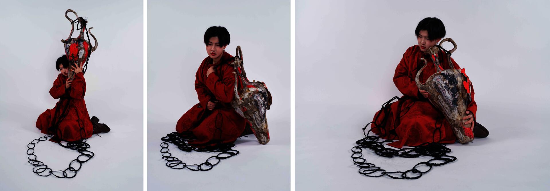 A model dressed in a red traditional Chinese Tang dynasty robe wears an oversized wine vessel jewelry piece. Looped black braided hair extends outward from the neck area, gradually increasing in scale until it surrounds the large vessel form.
