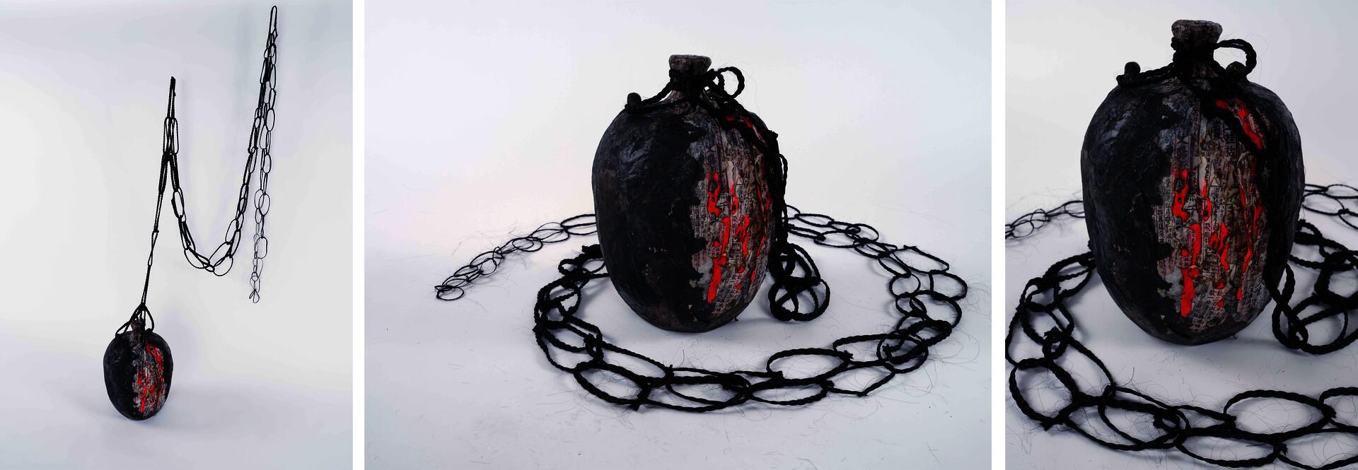 A large paper vessel with layered and burned edges sits low on the ground. The front surface is covered with overlapping fragments of Chinese poetry and textured paper layers, while the back has a smooth outer surface stained with black ink. Necklaces made from strands of dark hair surround the vessel.