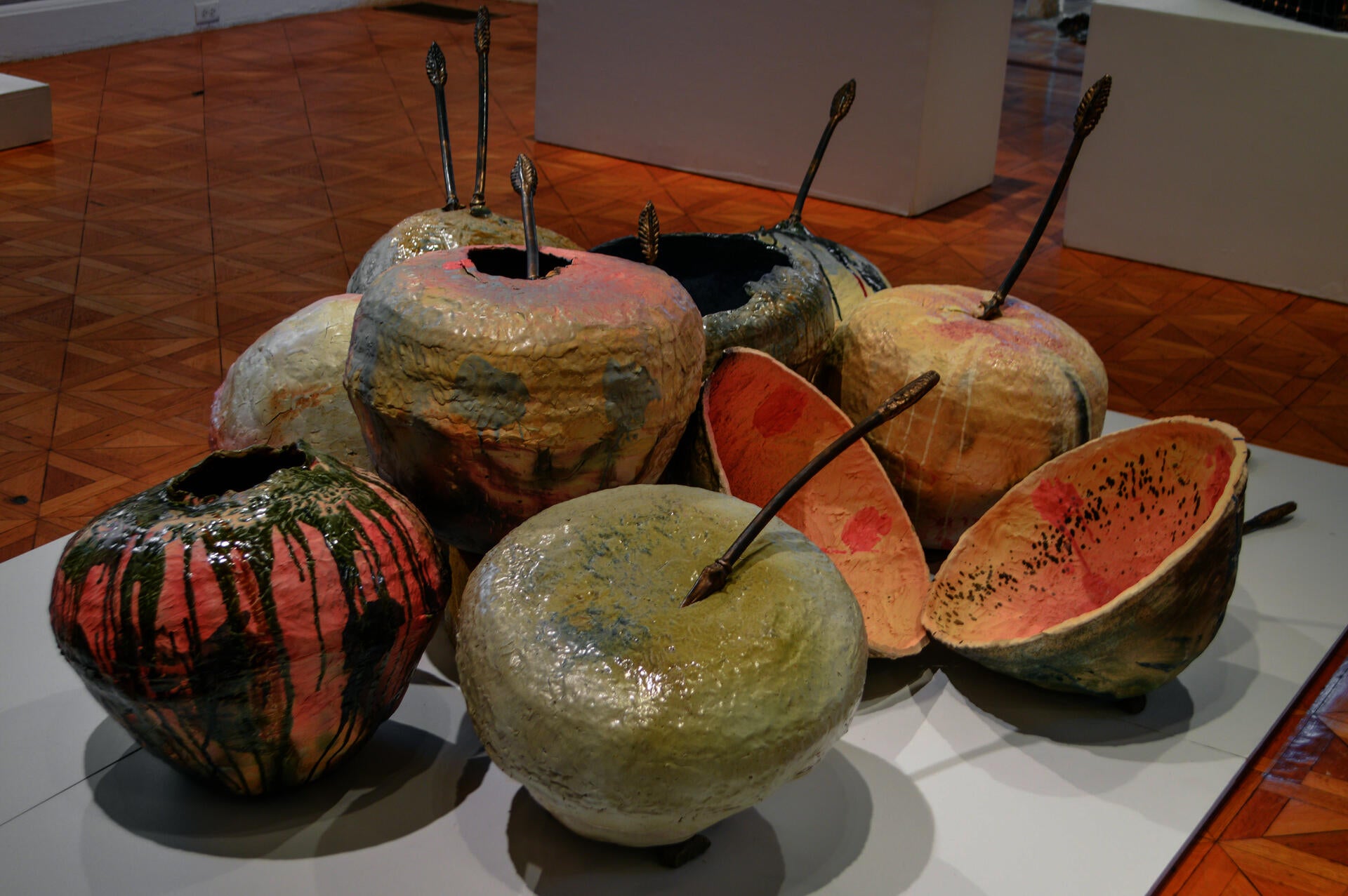 Ten multicolored ceramic spheres in a pile. Eight bronze-colored arrows protrude from the spheres. 