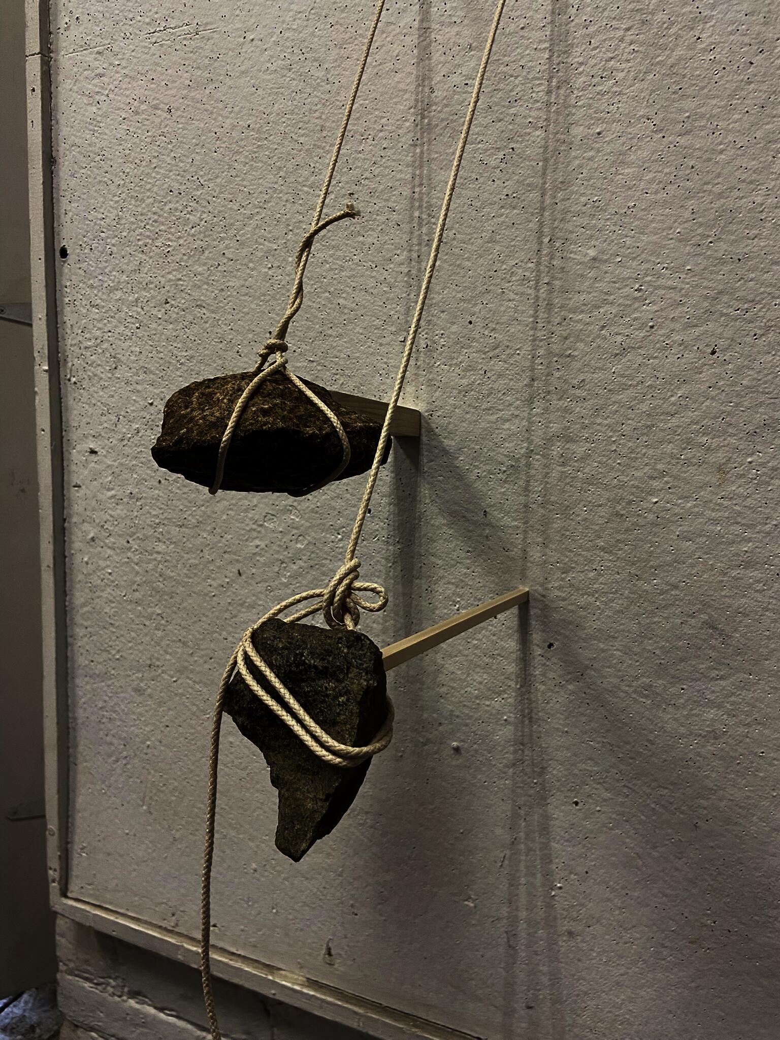 Two rocks hanging from ropes each hold a stick against the wall.