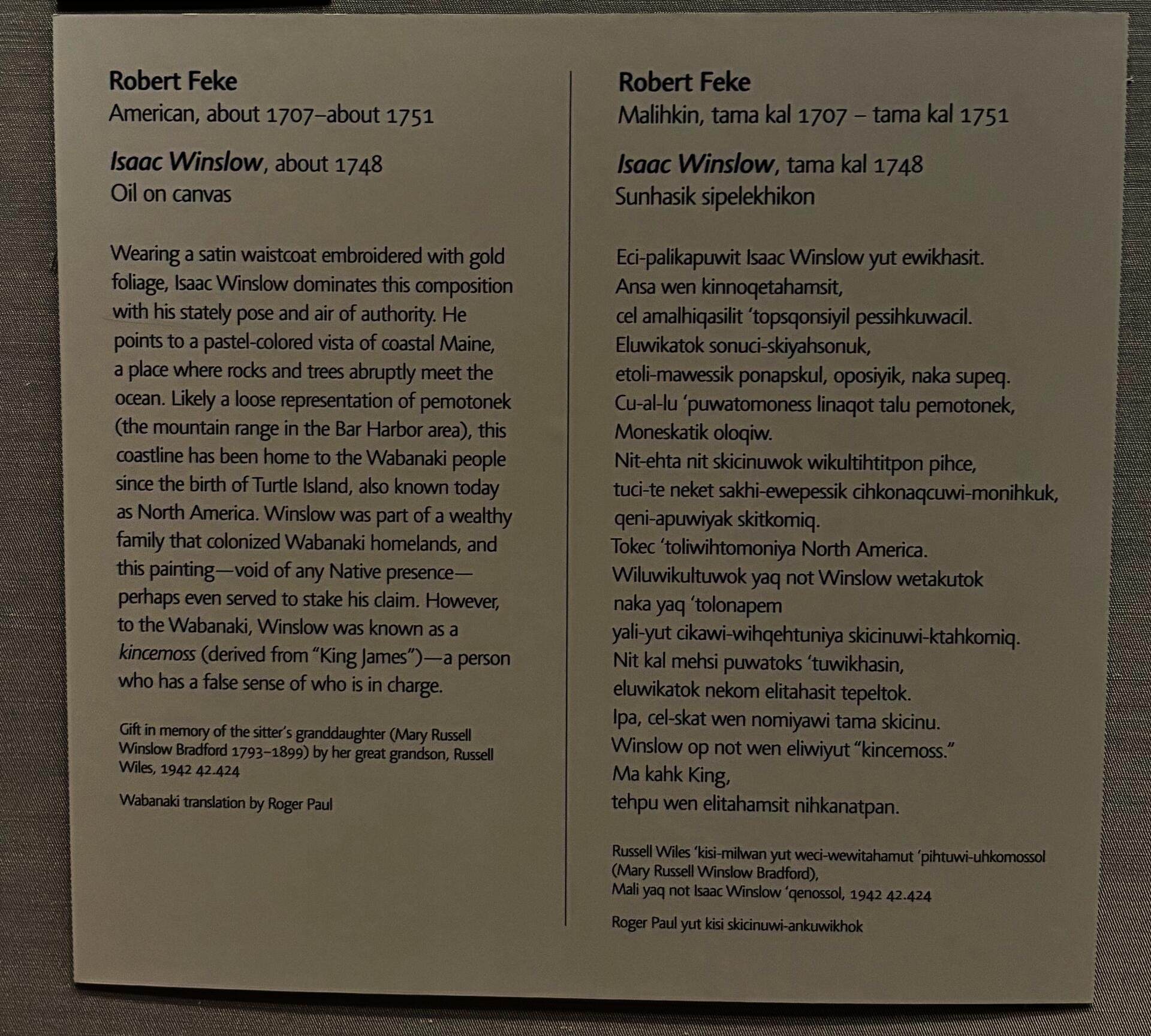 A gray label affixed to a gray wall, divided into two sections by a vertical line. On the left, biographical information about the artist, details about the painting, and a paragraph of interpretation are written in English. On the right, the same information is written in Wabanaki. 