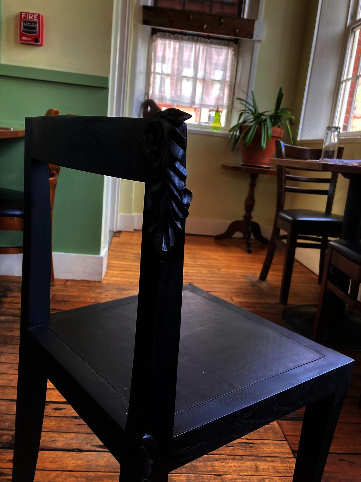Hand-carved wood chair leg detail featuring subtle leaf motif, demonstrating traditional chisel work applied to modern dining furniture
