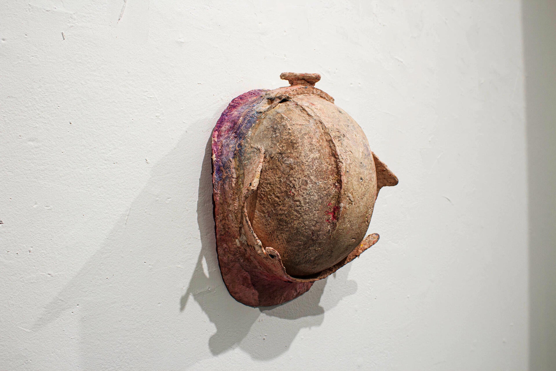 A construction worker's helmet covered by a crusty pink material. Hung flat on the wall.