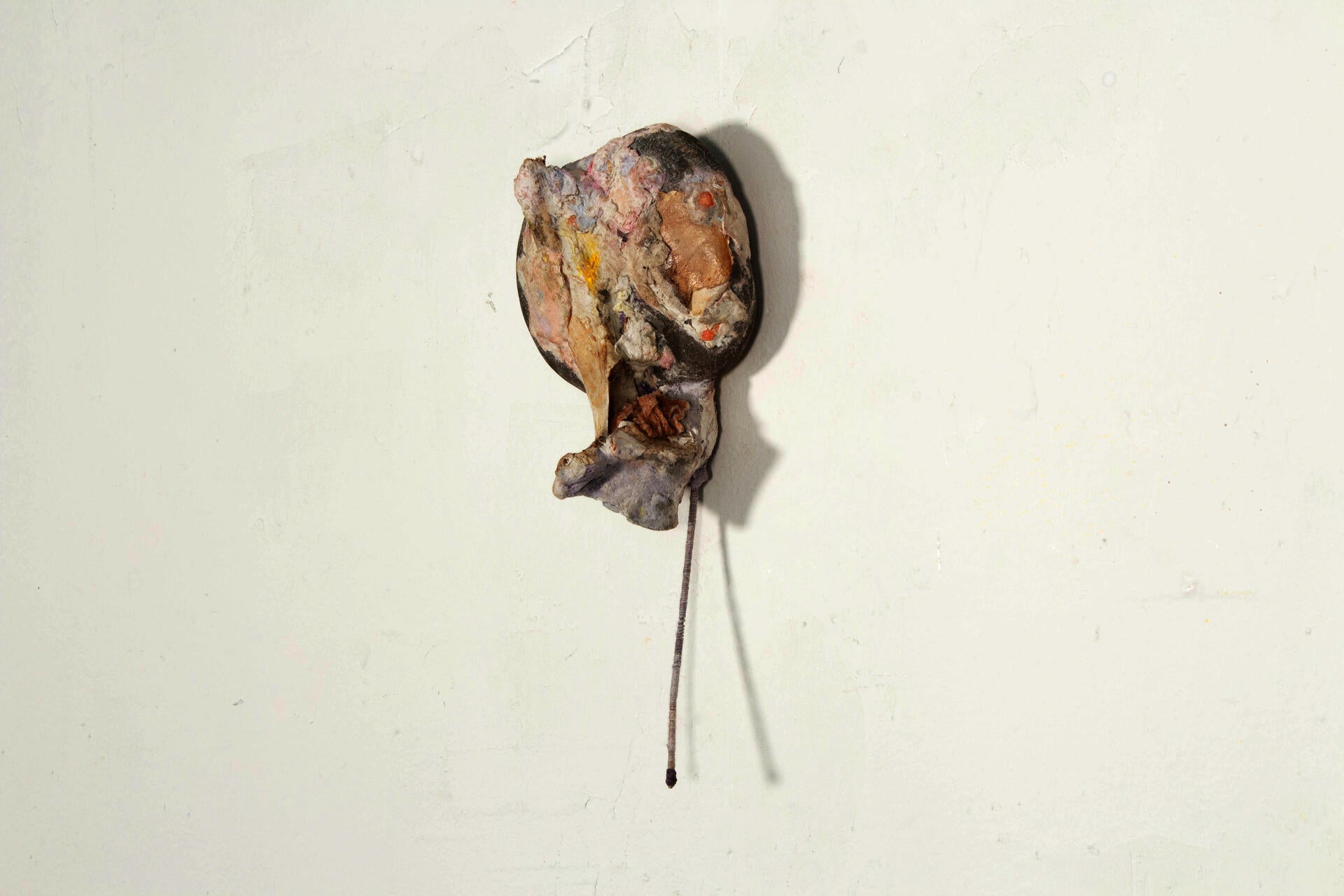 A hanging wall sculpture made with a rock covered by paper mache with a thin metal stem.