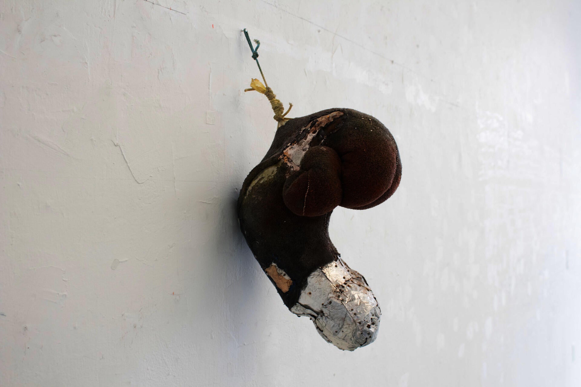 a twisted green neck pillow stiffened with glue. Its end is covered by squares of aluminum and nails, there are pins running along its seams.