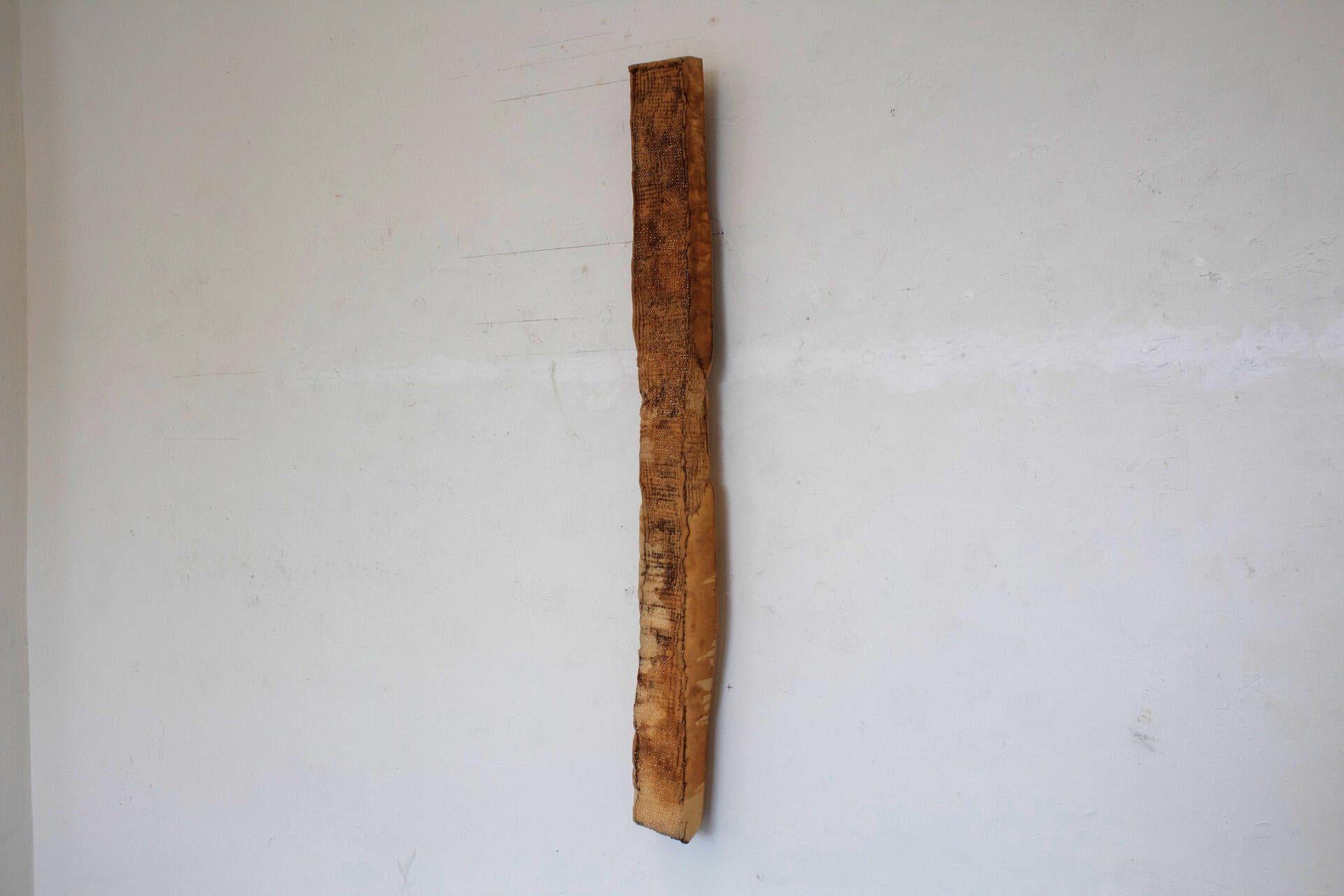 a long piece of foam covered in a grid of glimmering pins. Red ribbon necklace tied around the top of the piece hangs it from the wall so that it barely touches the floor.