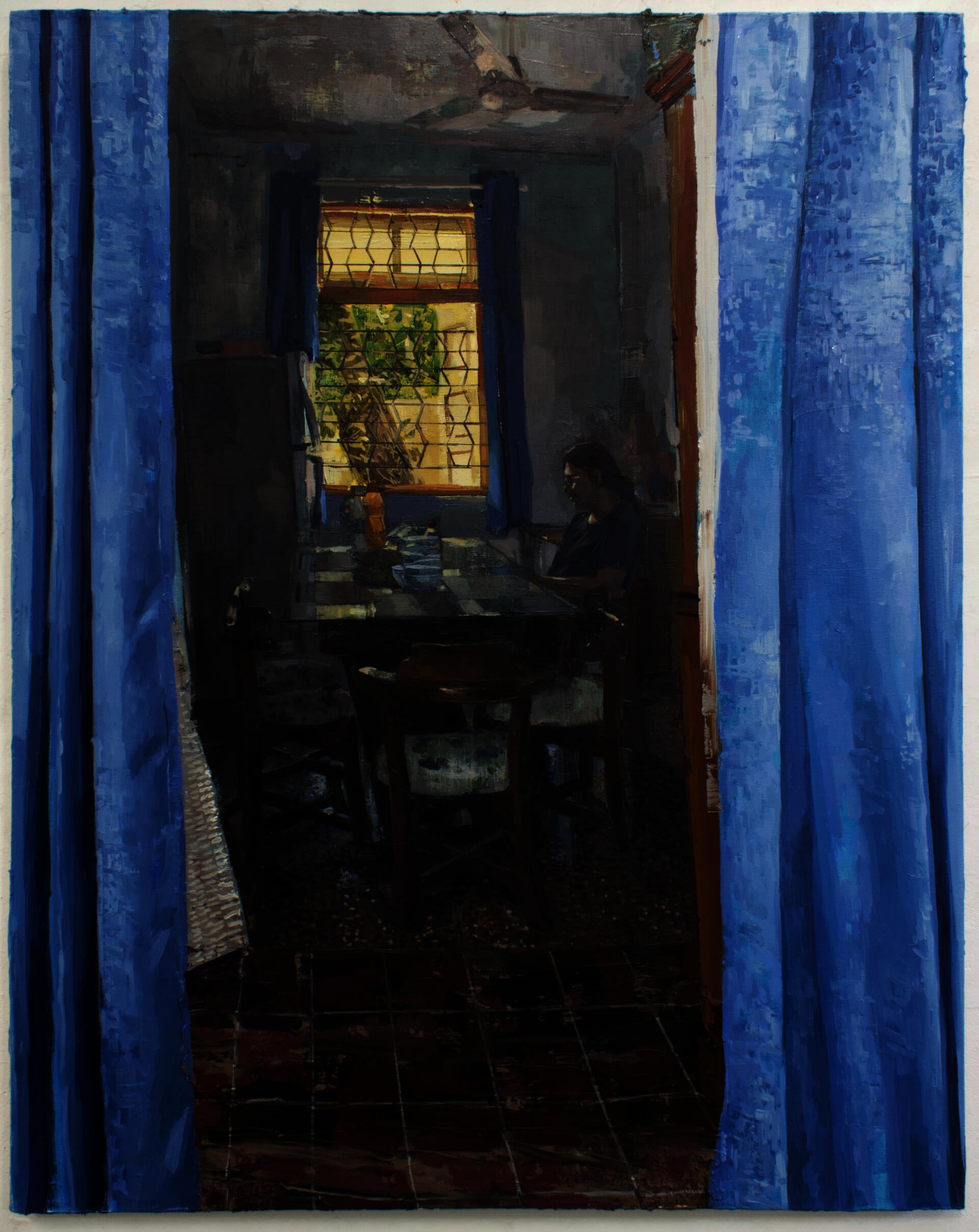 Figure sitting at a dining table next to a window being looked at through blue curtains.