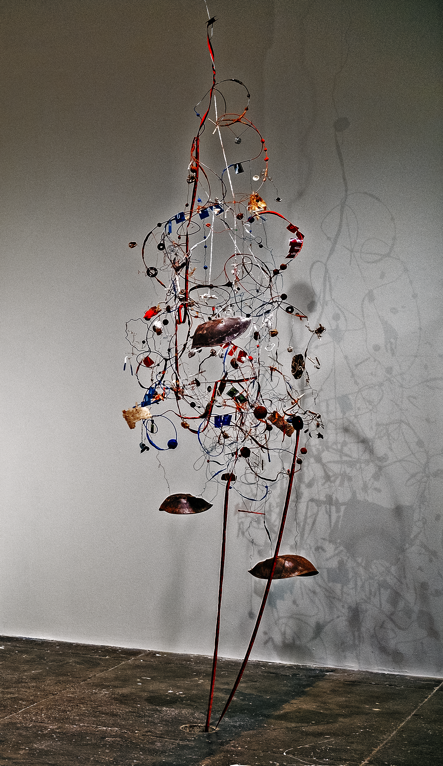 Found objects connected by wire and string, suspended from the ceiling. There is a black and red typewriter ribbon that unravels from top of the piece, disappearing through a hole in the floor.