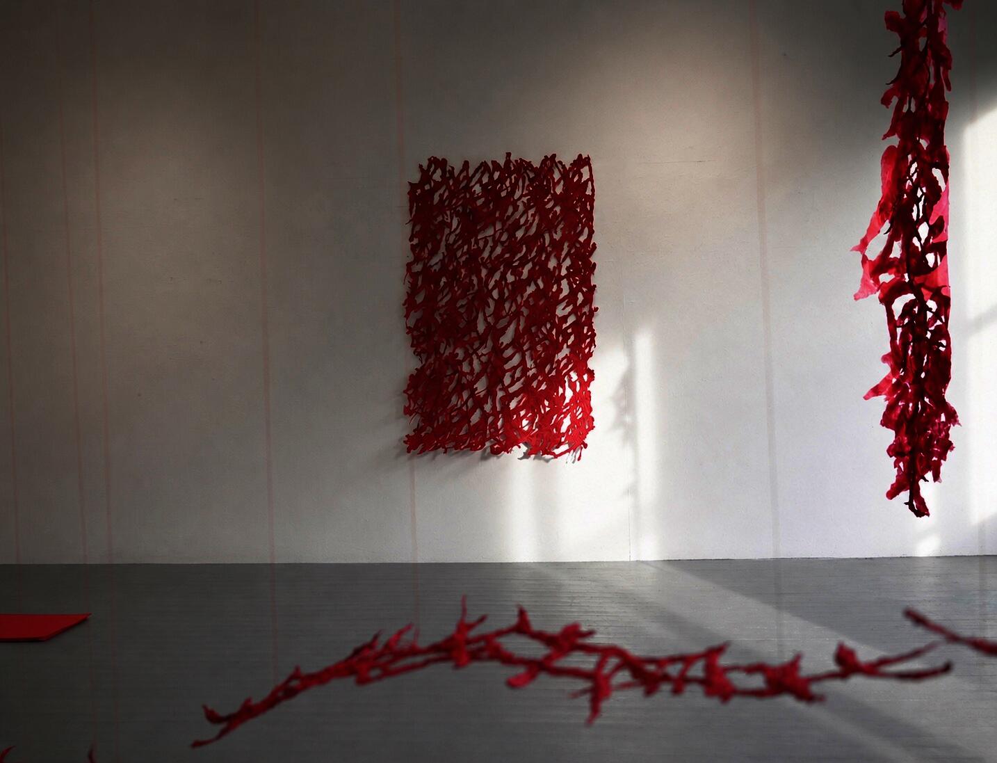 Red pulp painting installation hanging on a white gallery wall, with layered hanging forms.