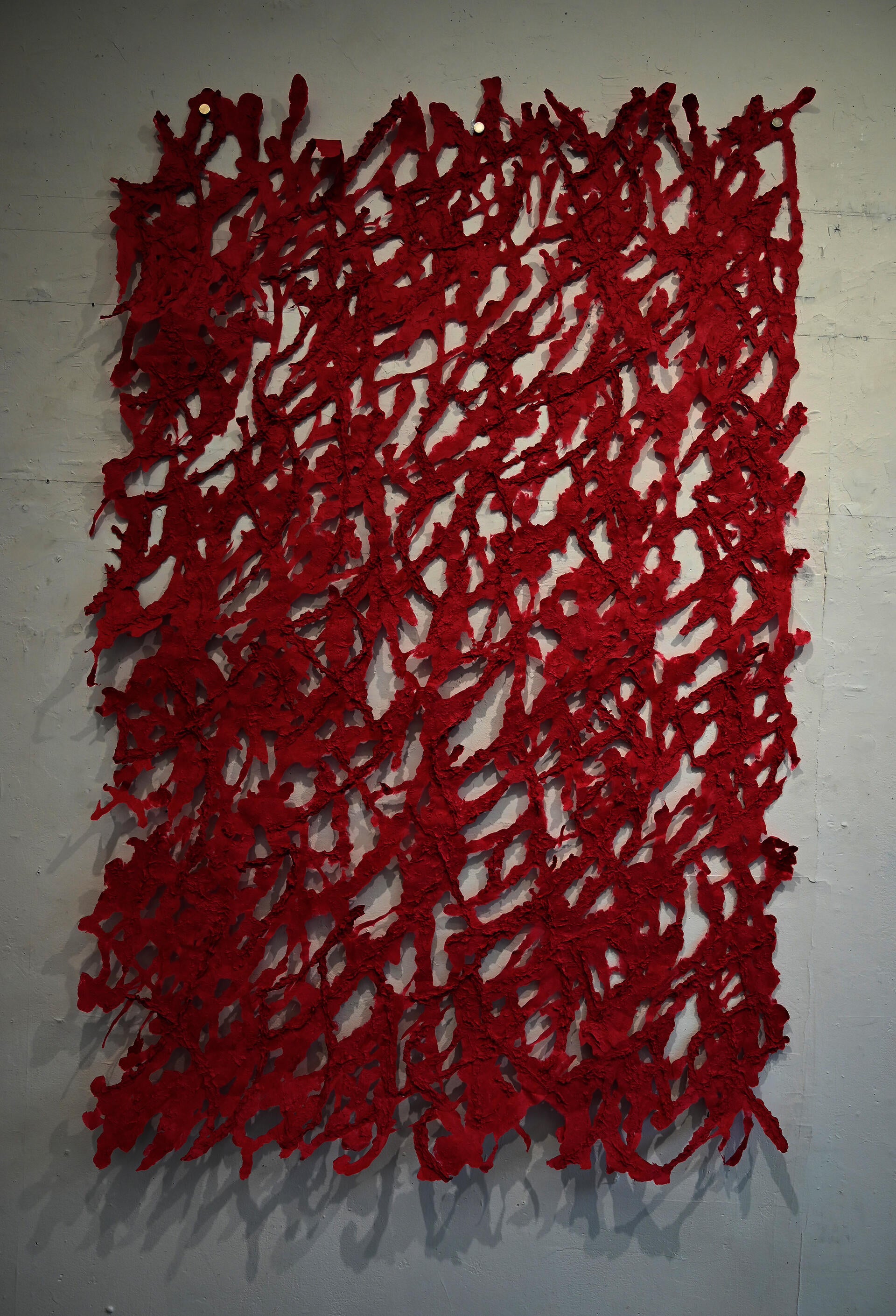 Web-like shape red pulp painting hanging on a white gallery wall