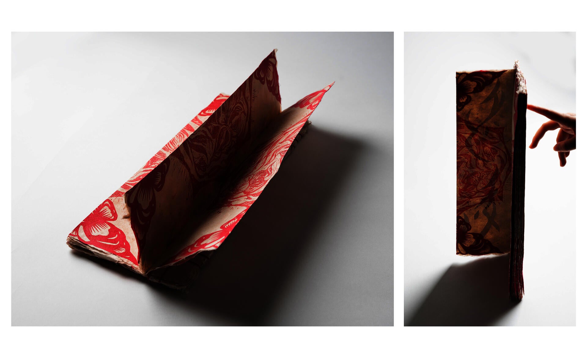 Handmade artist book with red floral prints, shown open and standing upright with a hand turning a page.