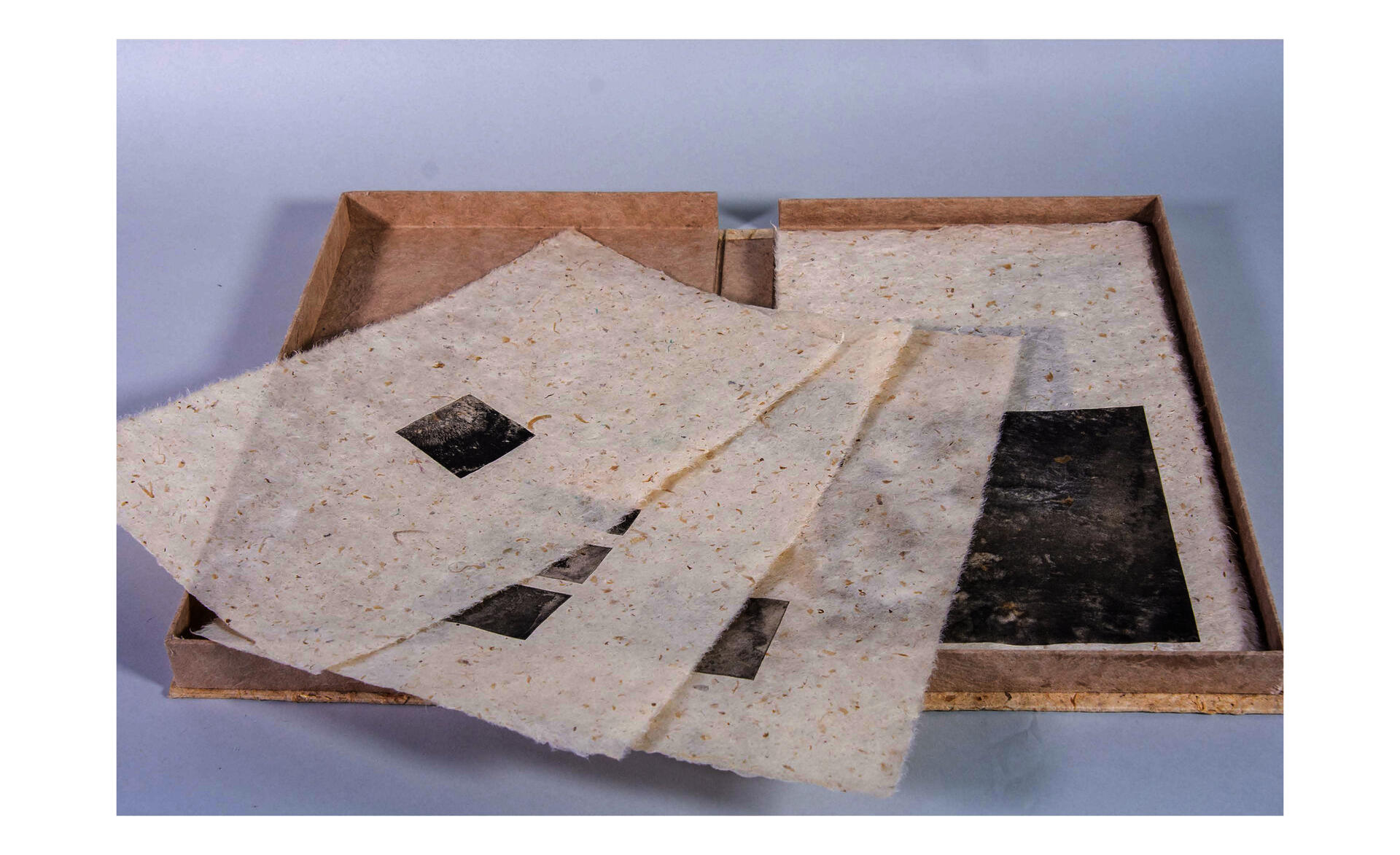 Handmade paper artist book in an open box, with layered pages containing black printed images.