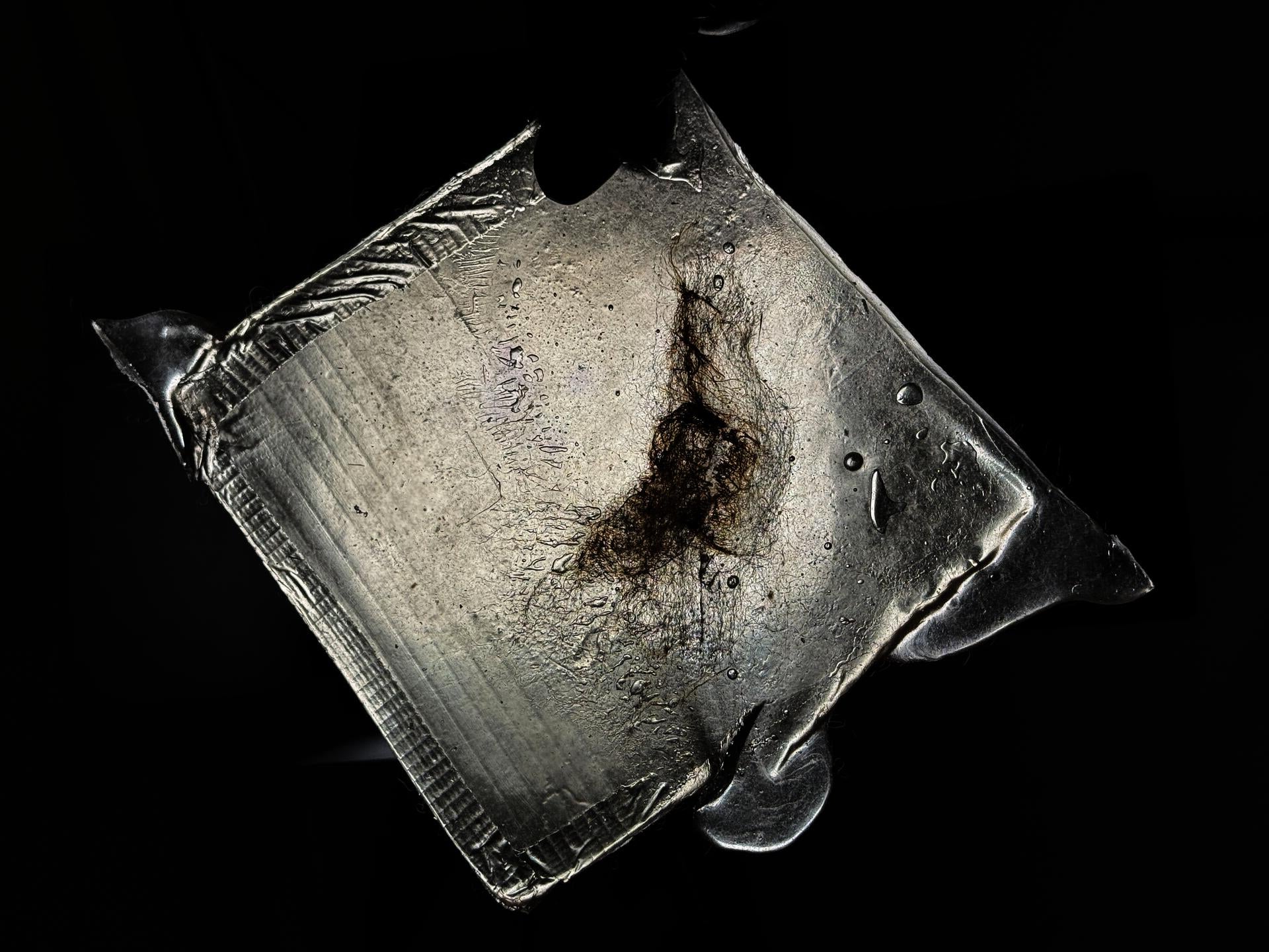 A bioplastic sheet made from a blend of wool and gelatin. 6 inches by 6 inches. The torn gelatin is heated until melted and then reformed. The charred wool reveals a distinct texture.