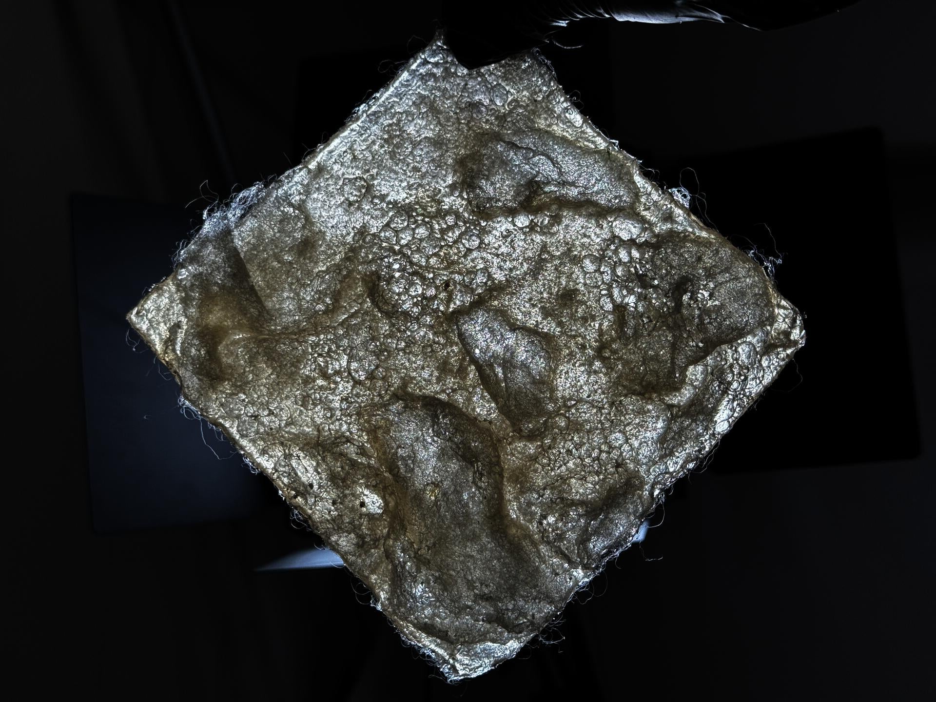 A bioplastic made primarily from wool and gelatin. 6 inches by 6 inches. Under this recipe and processing method, the surface develops large bubbles that can be pressed and spring back, forming a cross-linked network structure internally. It is translucent with a slight yellowish tint.