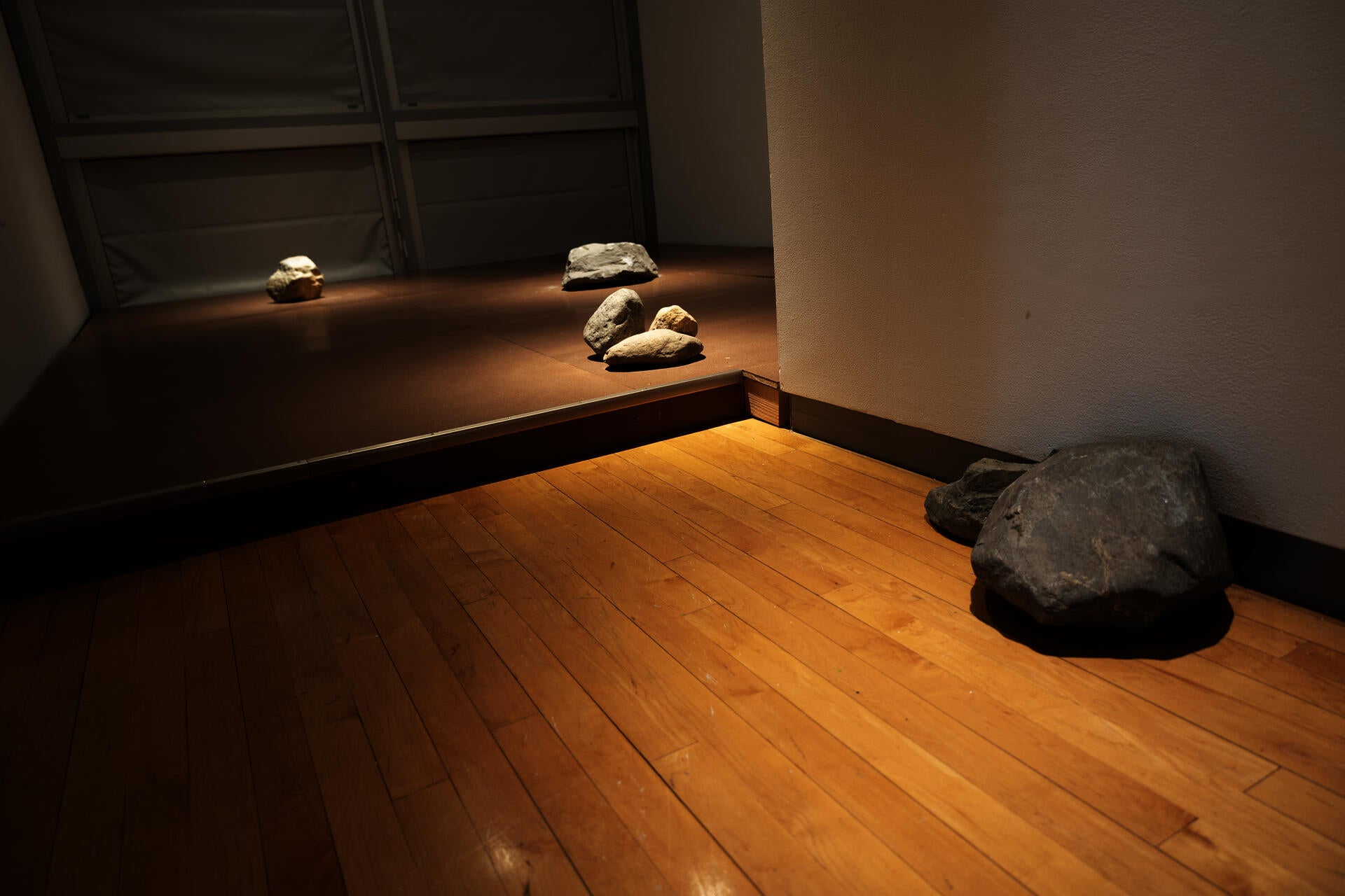 A brown, raised flooring with 4 groupings of large rocks. The rocks are lit from above, highlighting their presence on the flooring. 